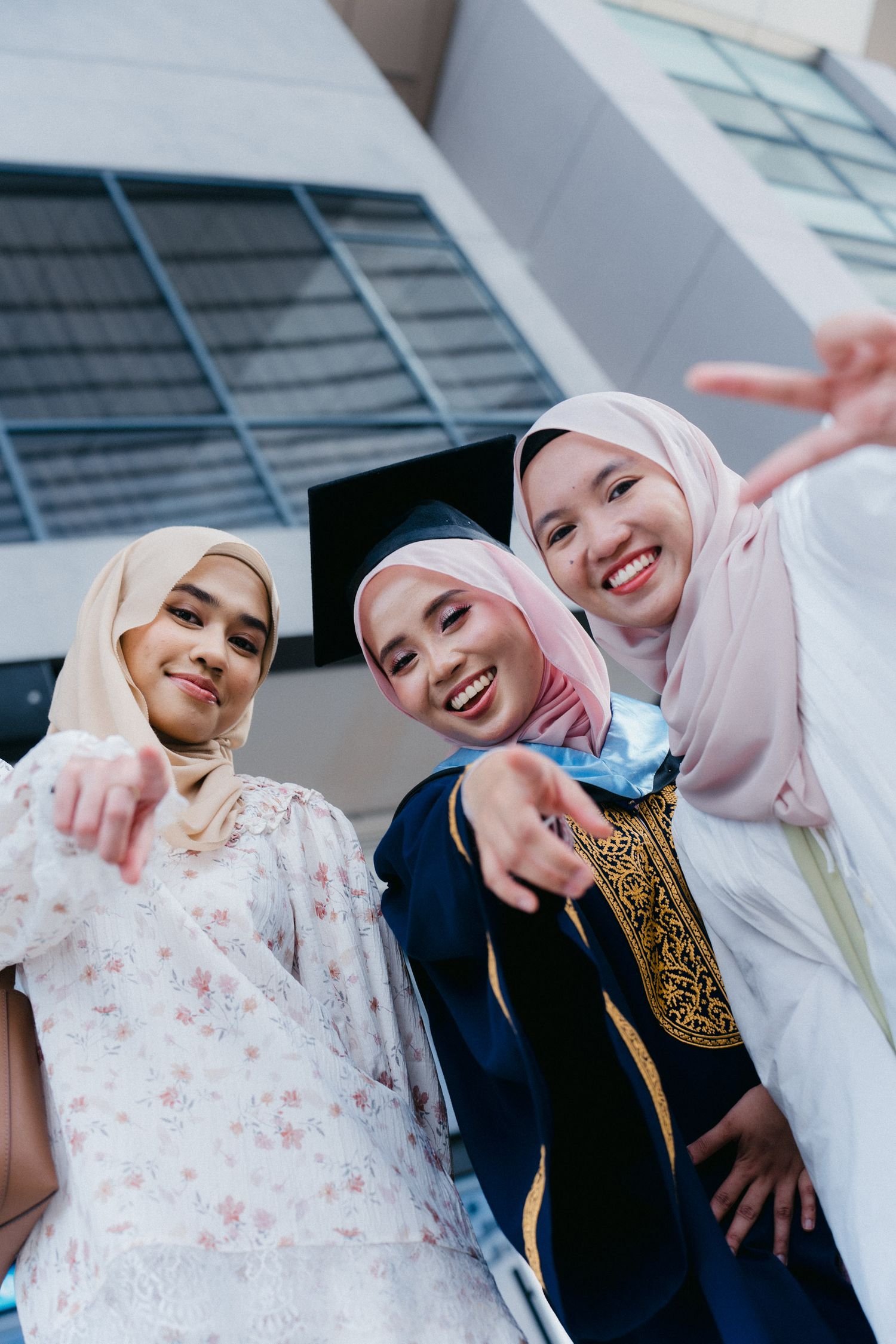 Three friends in hijabs and traditional clothing pose playfully together in a modern building setting.