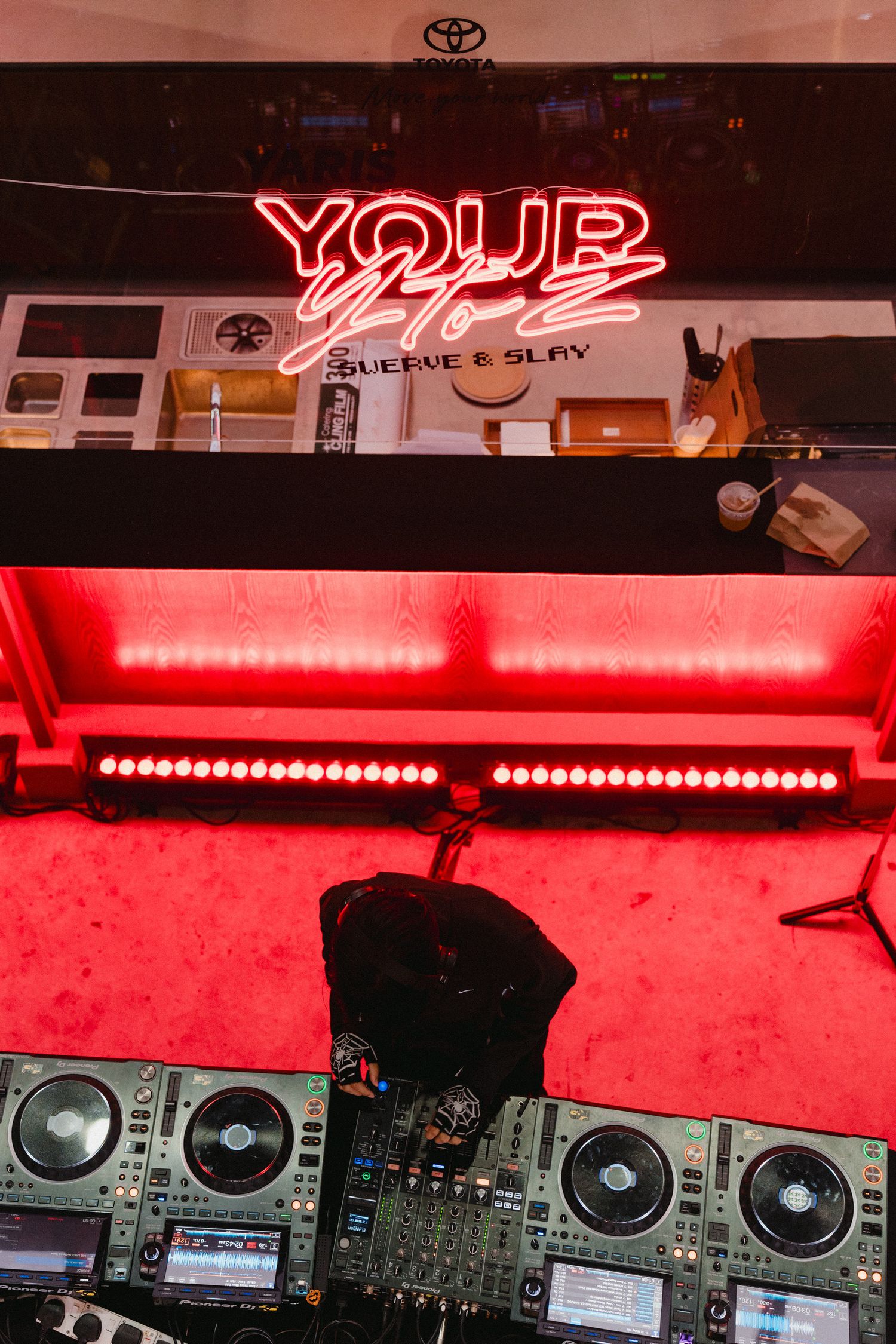 Professional DJ equipment setup with multiple turntables and mixers illuminated by red lighting at a nightclub venue.