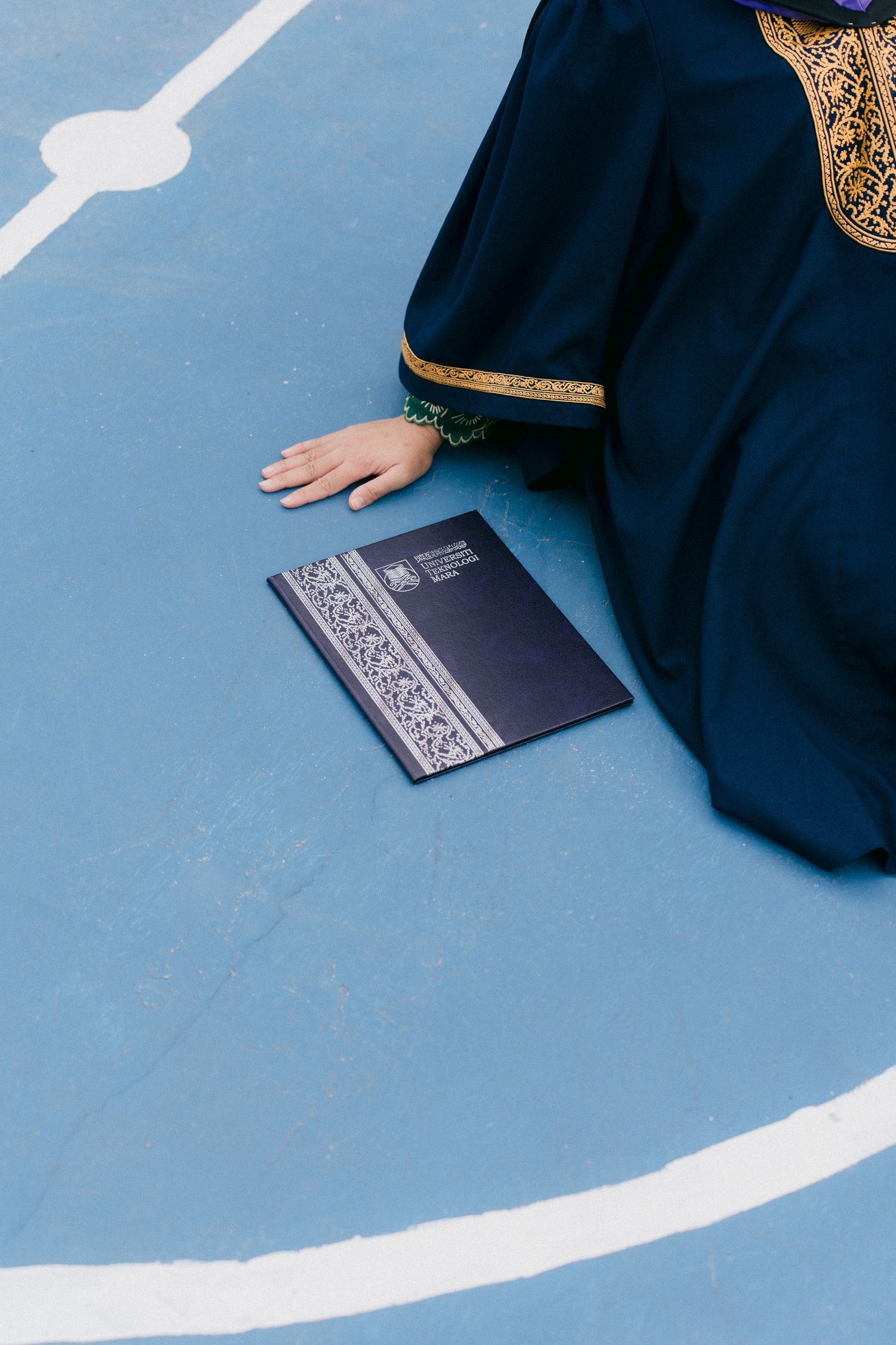 Black book with ornate silver pattern cover lies on light blue surface with dark fabric visible in corner.