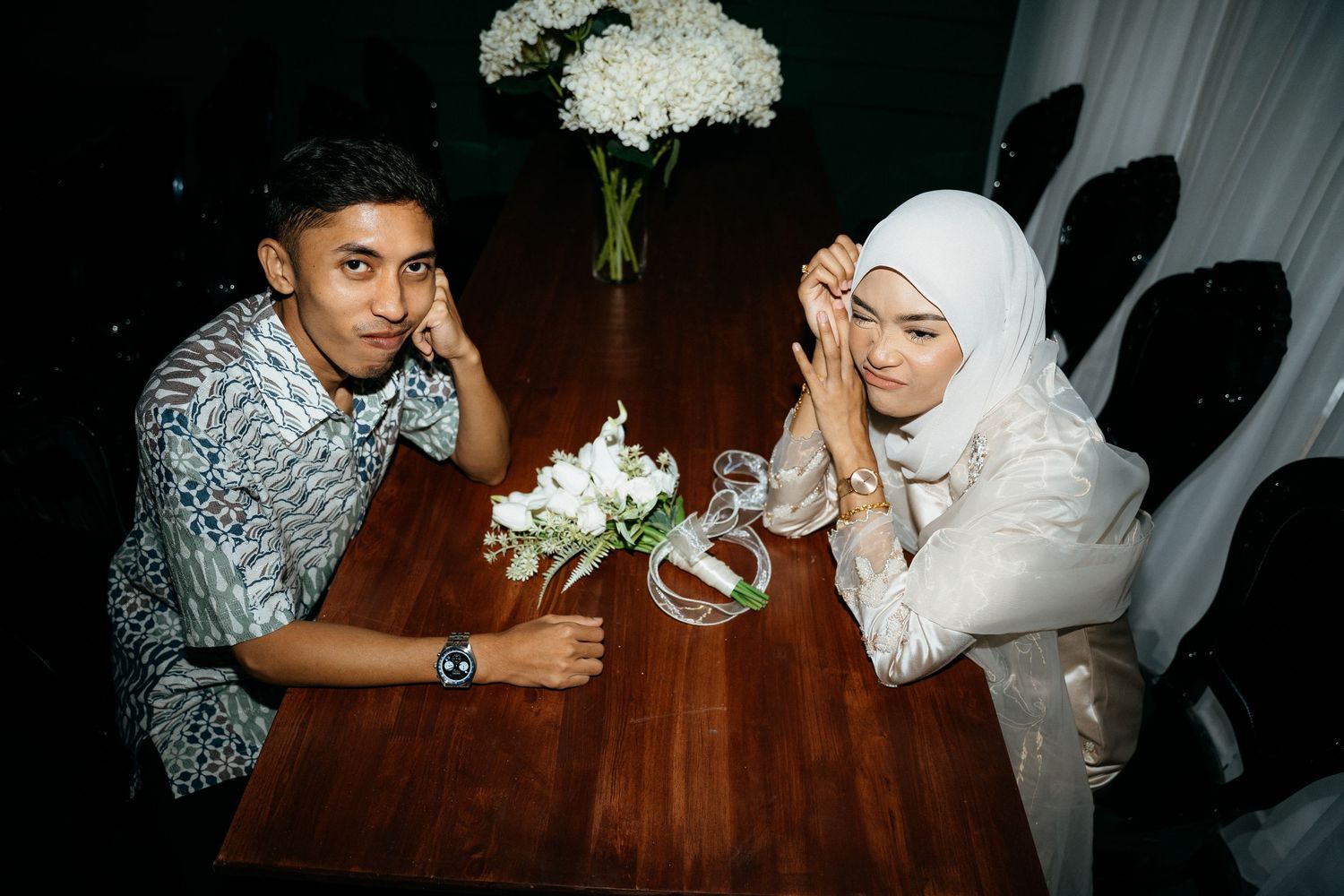 Couple celebrating their wedding with traditional Malaysian customs at an ornate indoor ceremony.