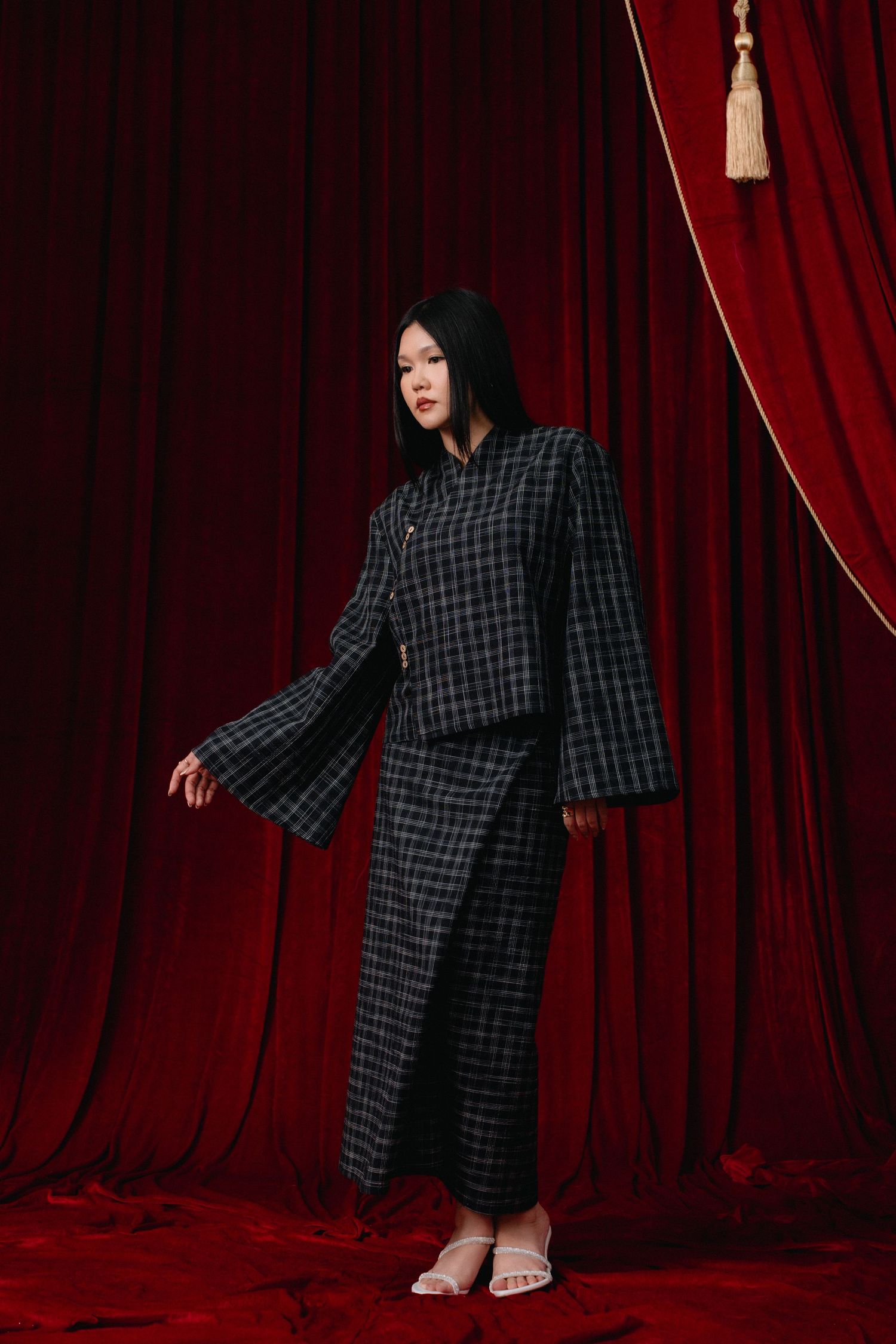 Person in checkered kimono-style dress poses dramatically against red velvet curtain backdrop in multiple poses.