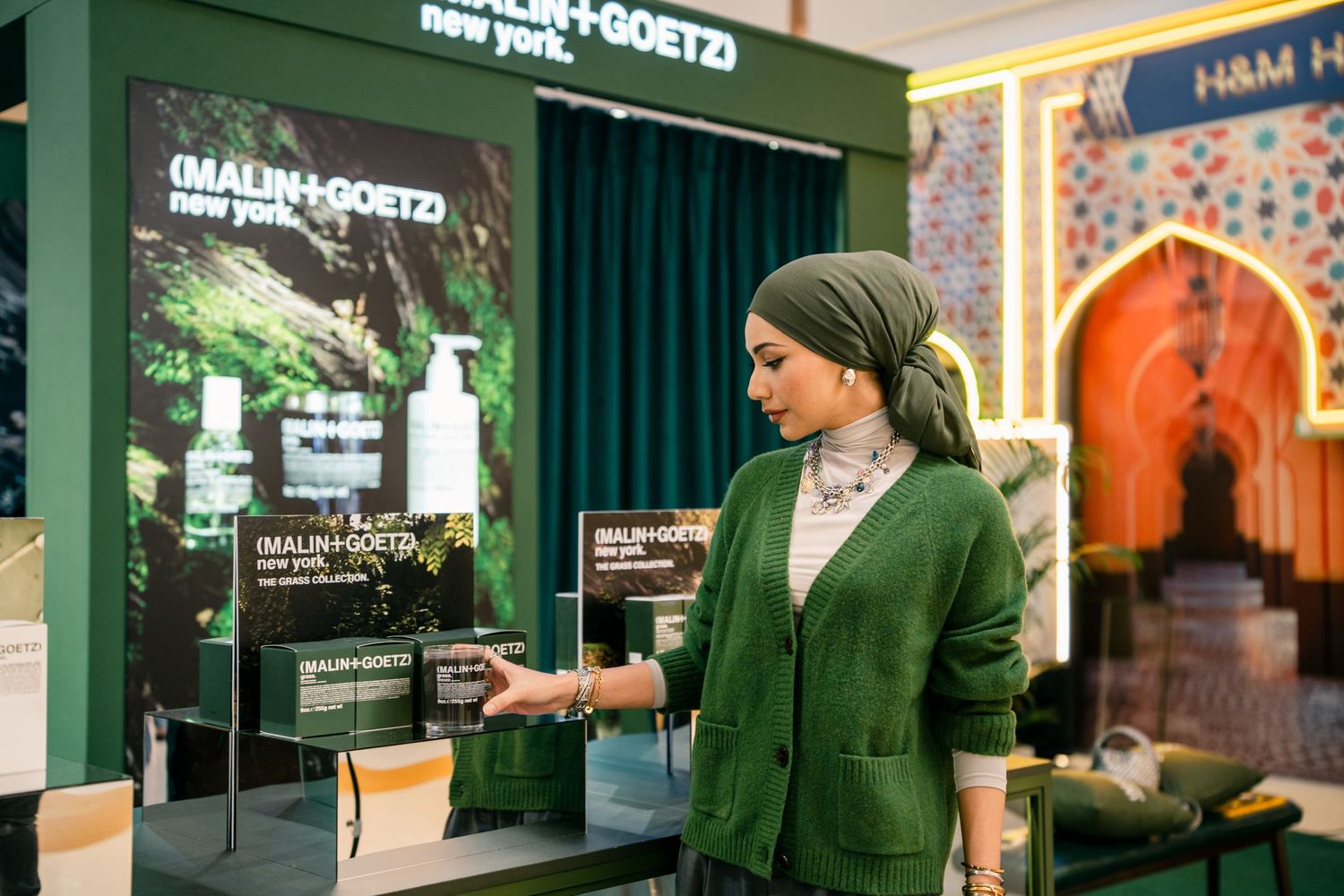 Malin+Goetz retail display with green curtains and product signage in store setting.
