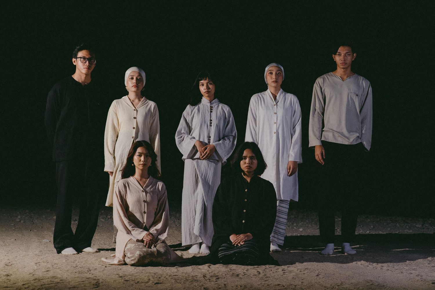 Group photo of seven people in monochromatic clothing against a dark background.