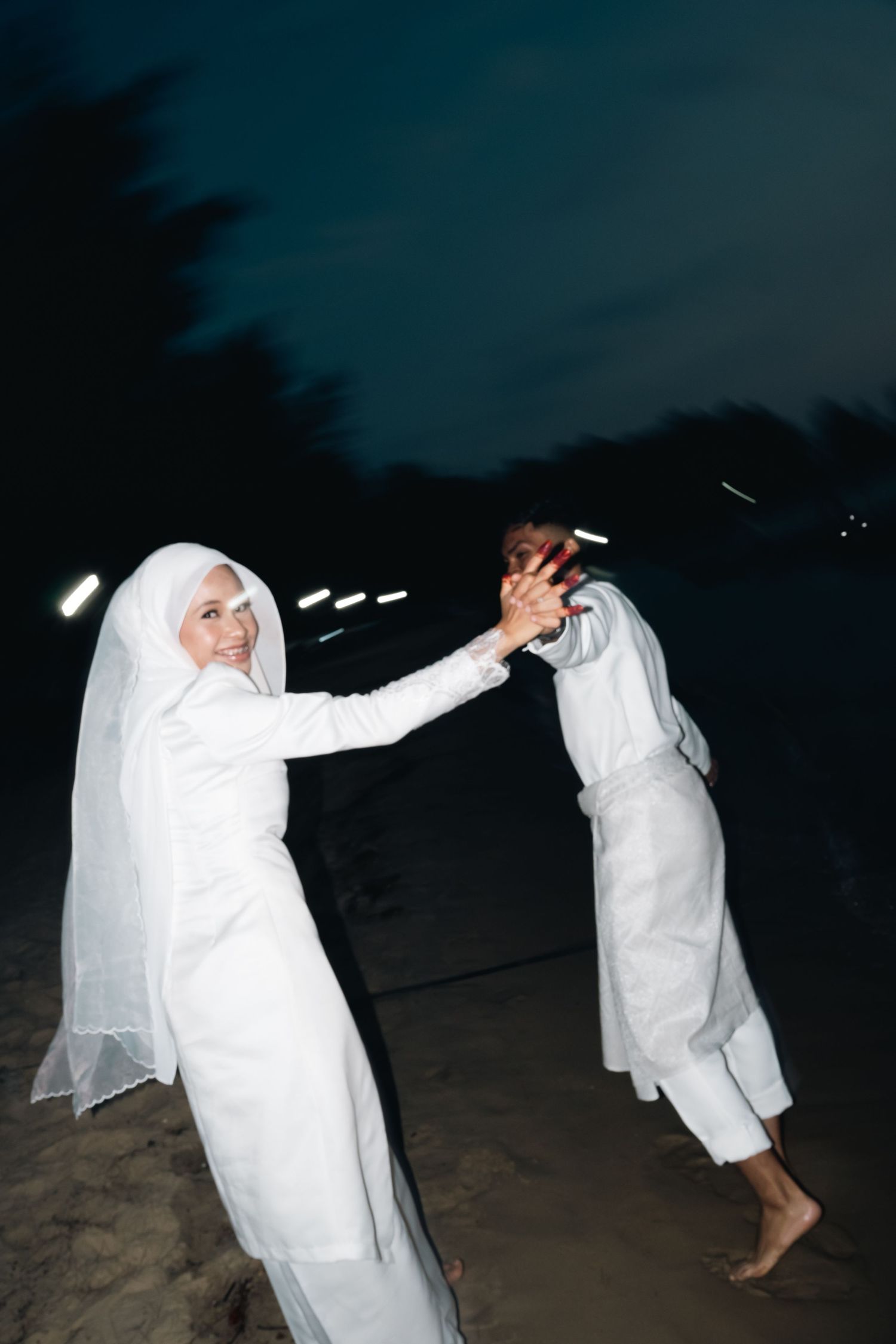 Two figures dance playfully on a dark beach while wearing white sheets as ghostly costumes in the night.