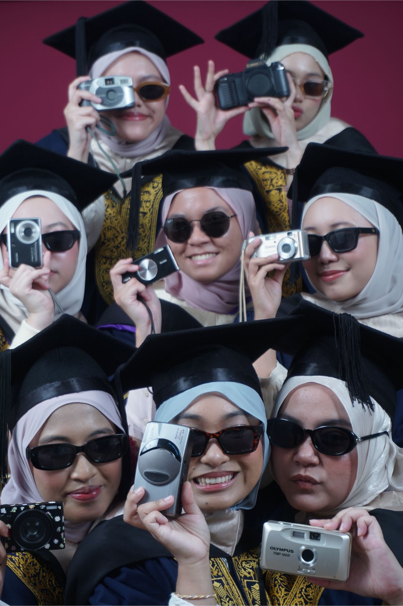 Group of female graduates in hijabs and caps holding cameras, smiling at graduation ceremony.