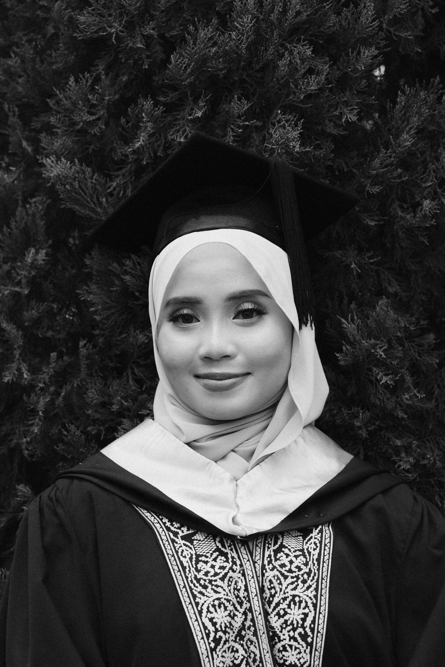 A series of black and white portraits showing a person in a white hijab and black embroidered garment against a dark background.