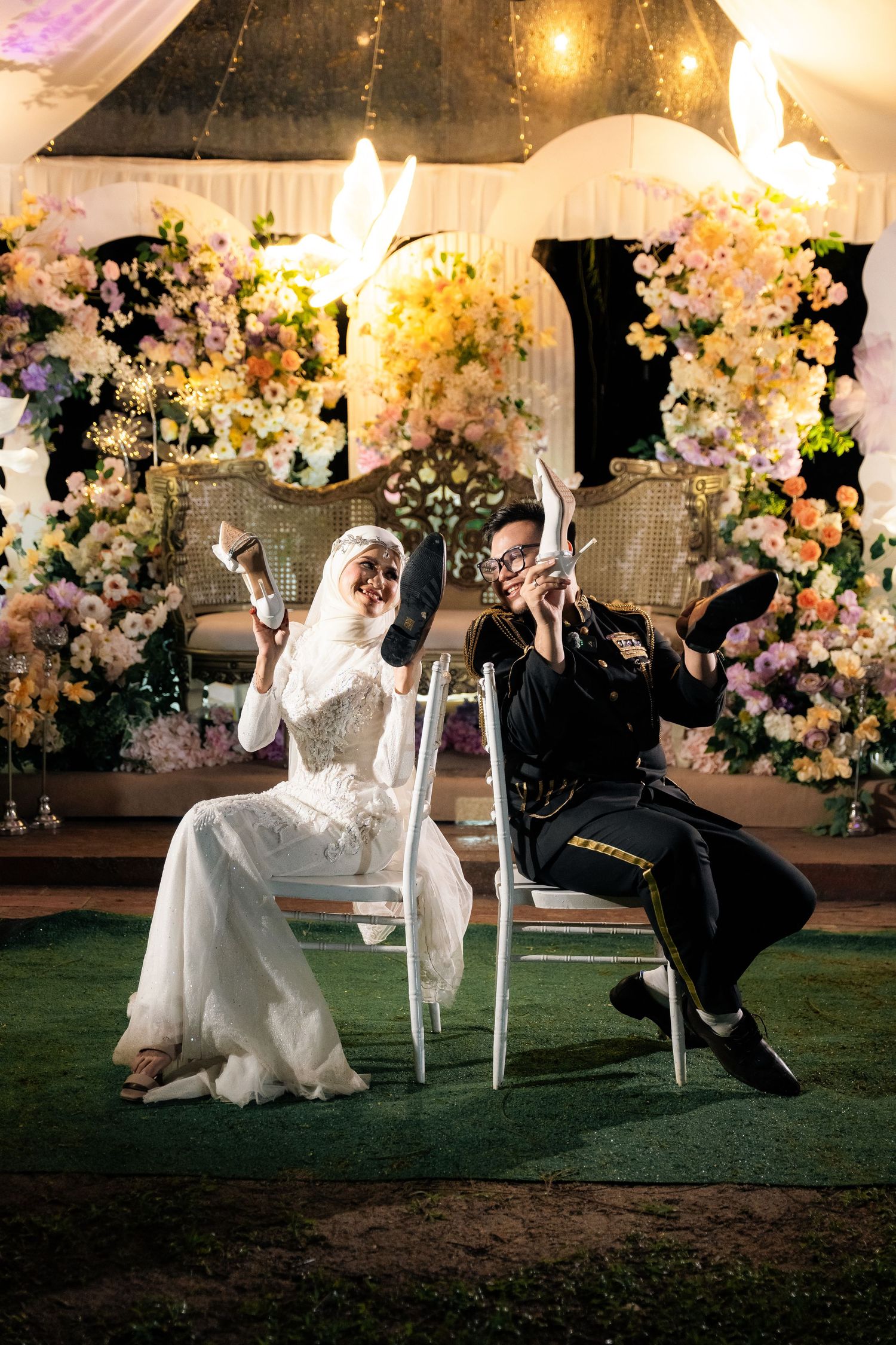 Wedding party performs martial arts moves on lawn at evening reception with floral decorations and string lights overhead.