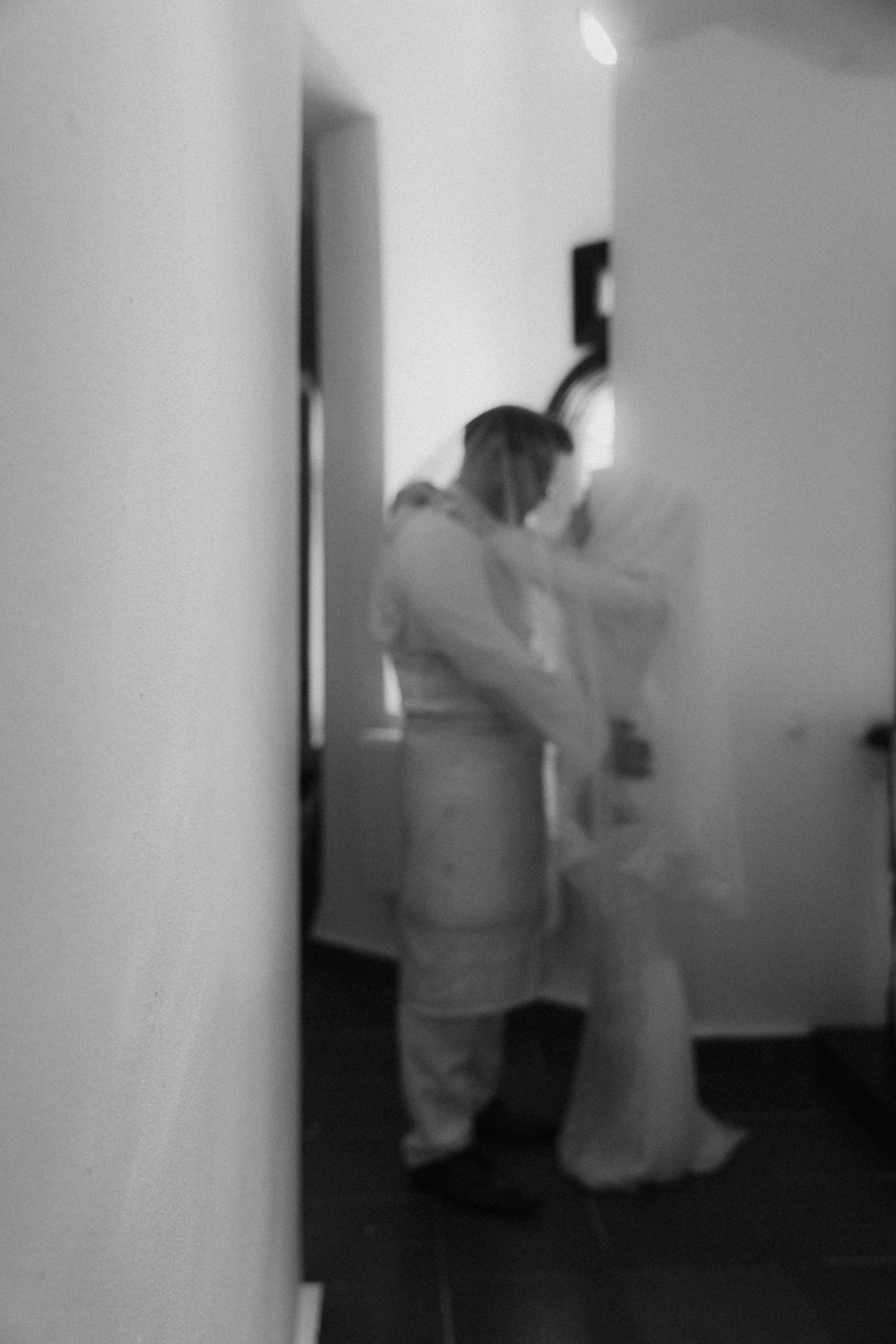 Blurry black and white photograph showing two figures embracing in a hallway interior.