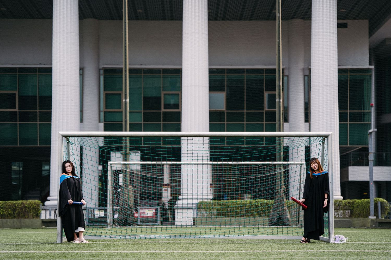 Students in graduation attire standing on opposite sides of a volleyball net at a university sports facility.