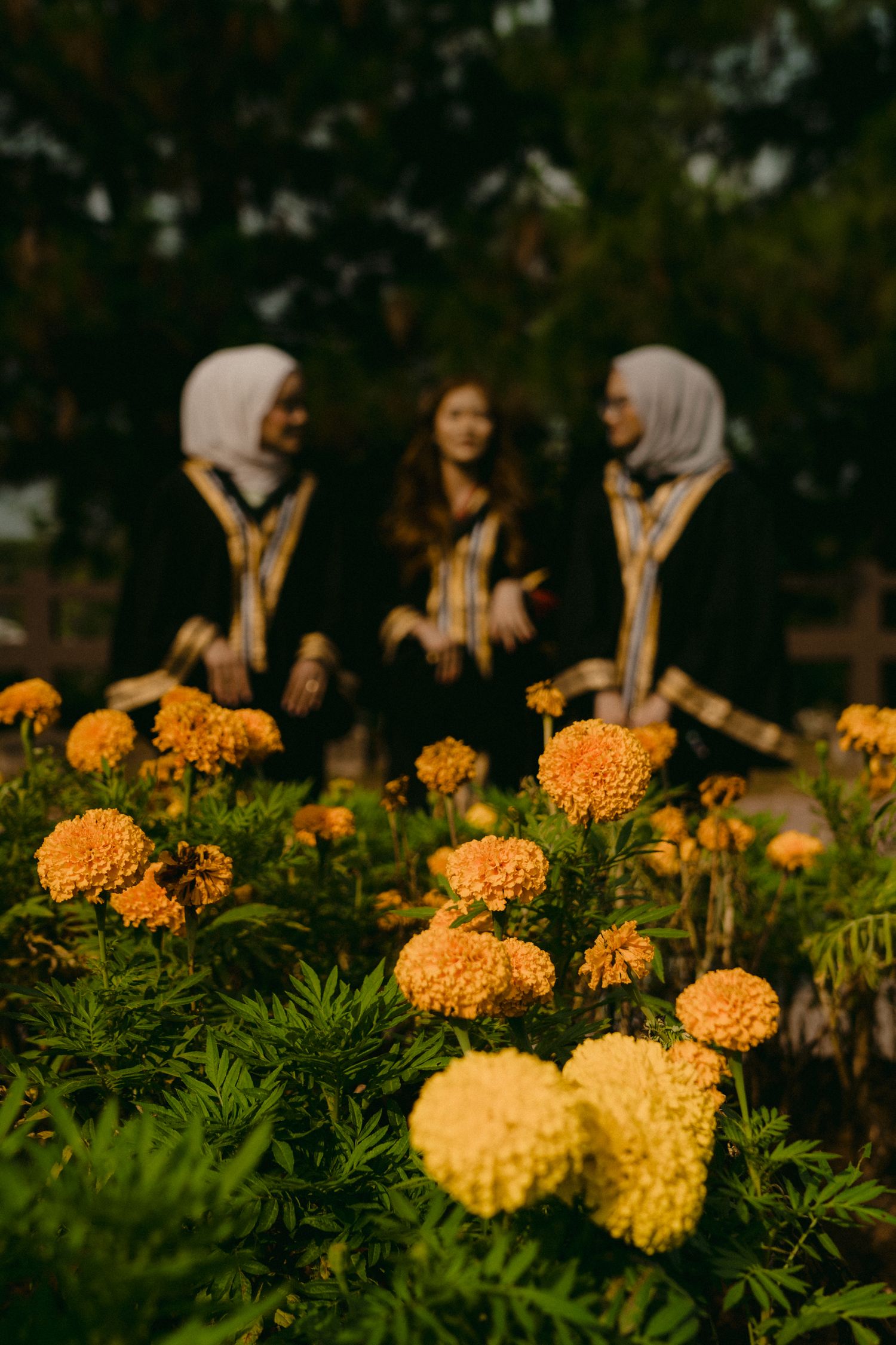 Three people chatting near vibrant orange marigold flowers in a garden setting.