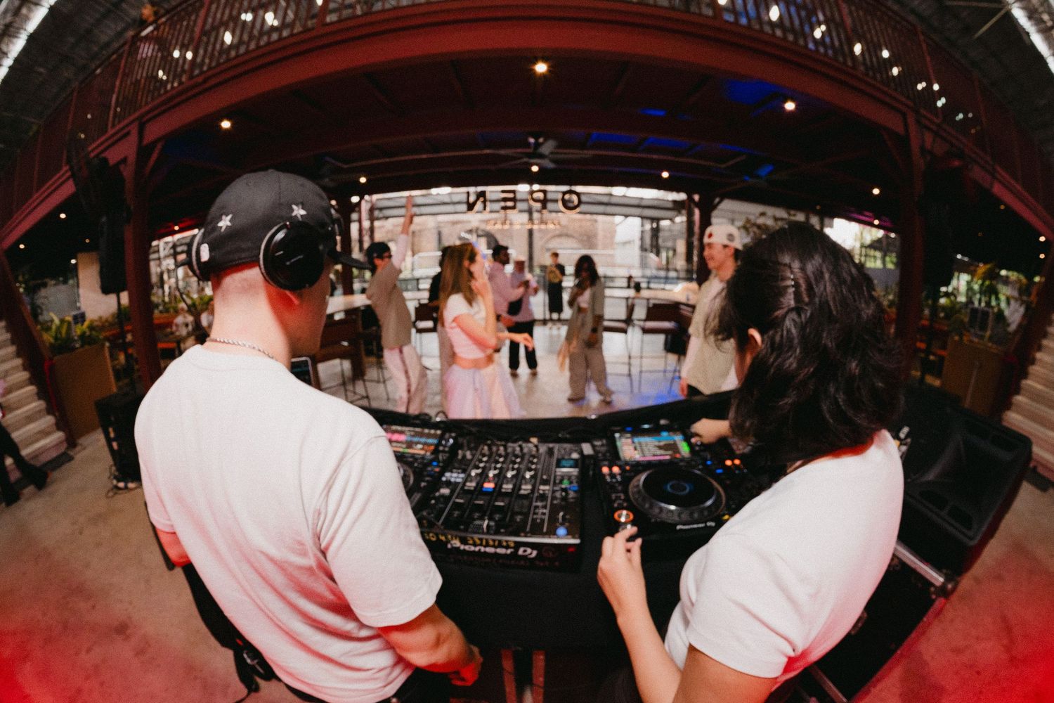 A DJ performs at a nightclub with turntables and mixing equipment while the crowd dances in the background.
