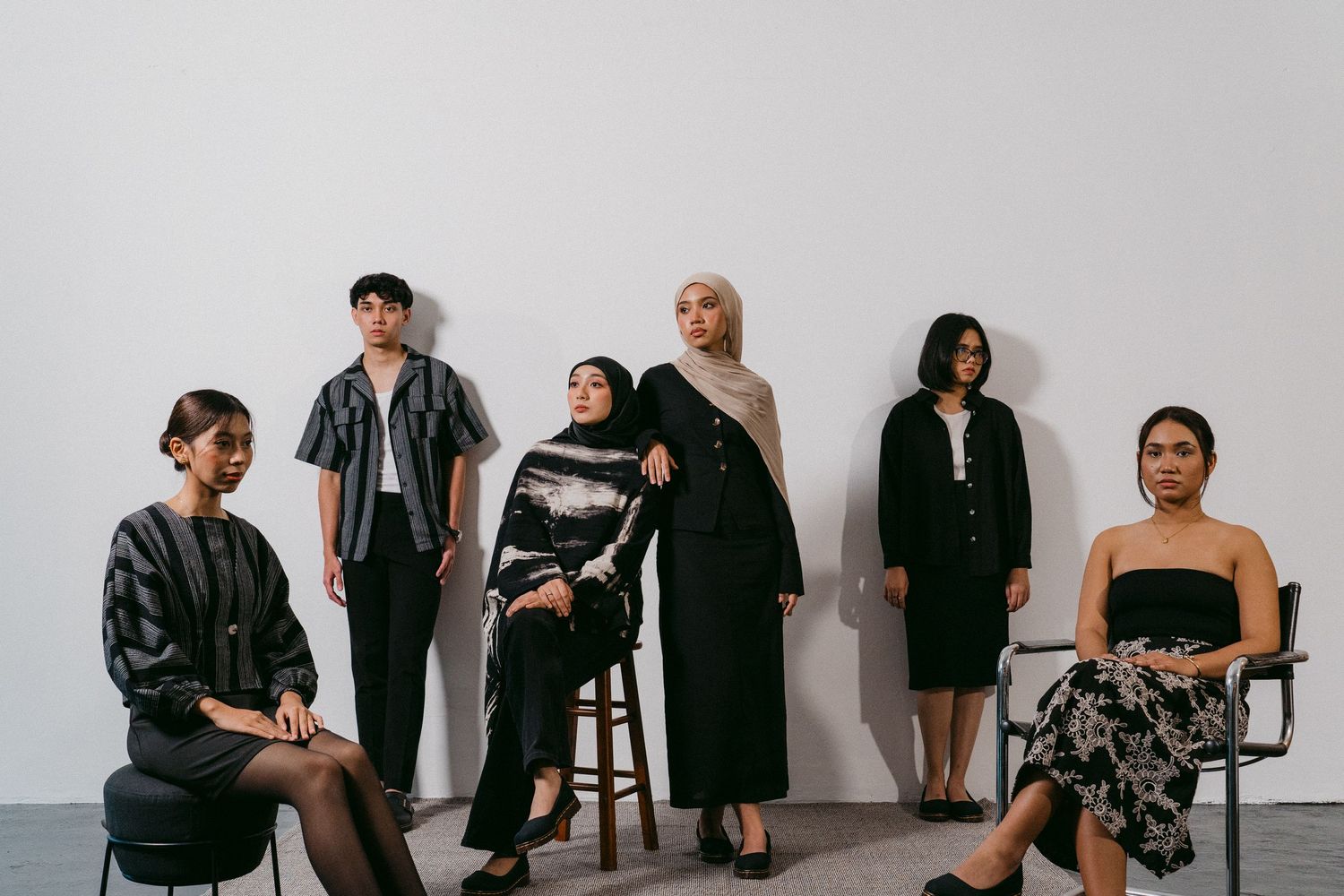 Group photo of models in modern black and neutral toned outfits against white studio background.