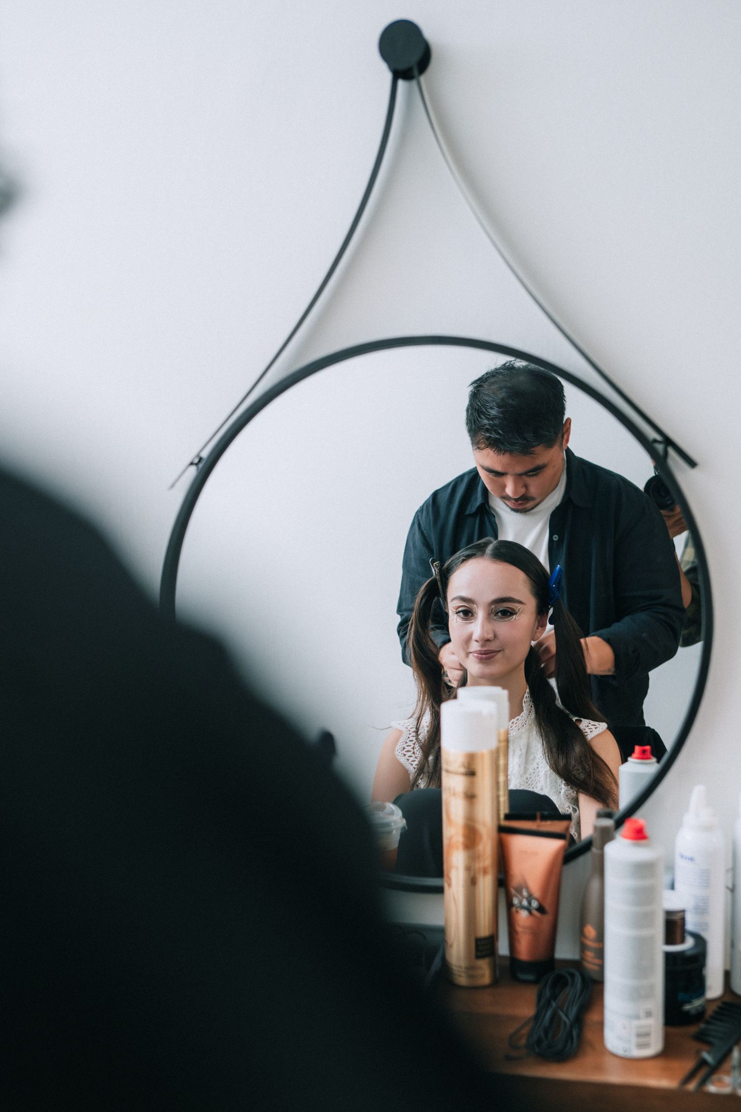 Behind-the-scenes photo of beauty preparation in round mirror at fashion event.
