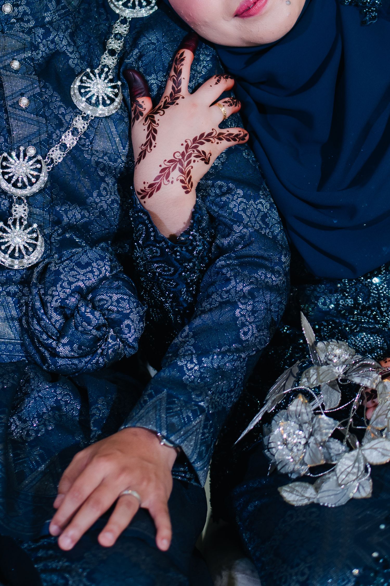 Close-up details of decorative henna designs on hands against dark blue traditional clothing.