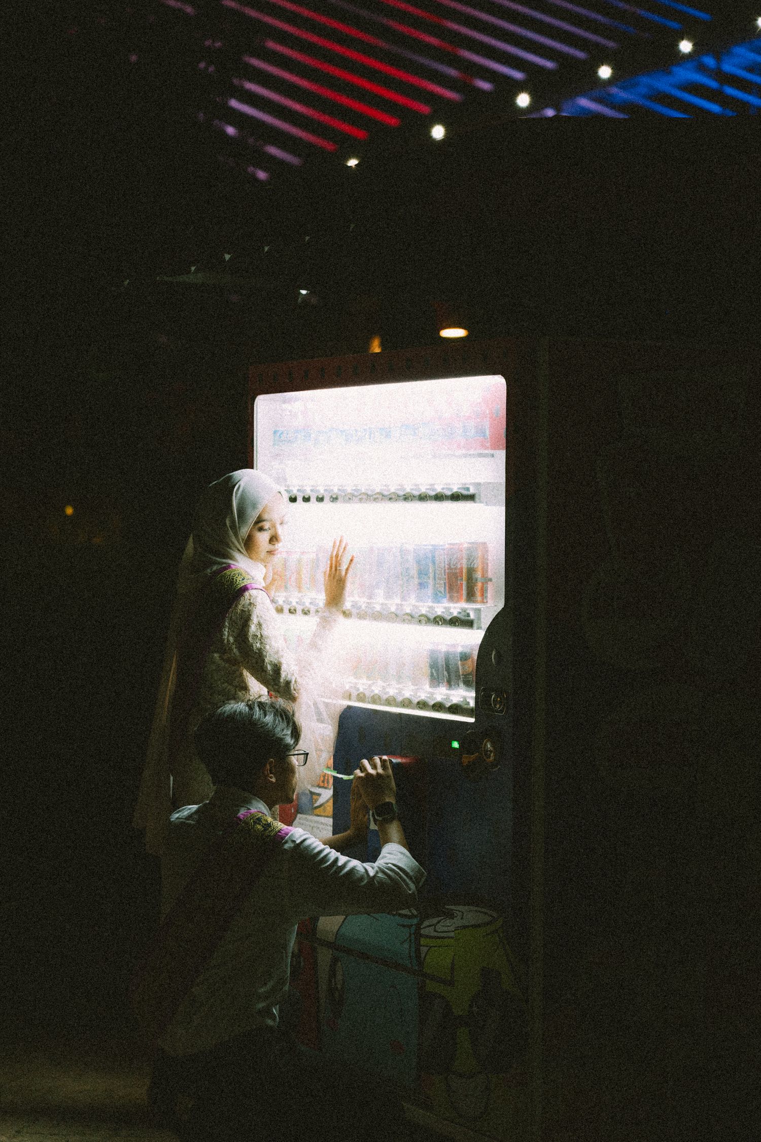 Figure in hijab sits at illuminated display in dark environment.