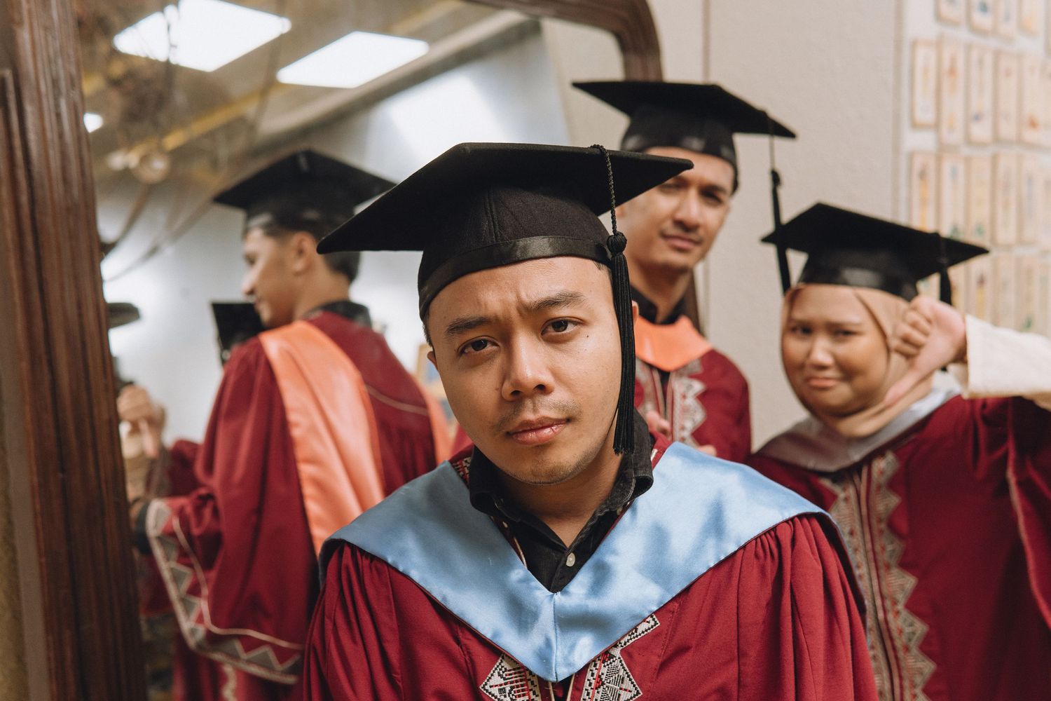 A group of graduates in red and blue academic regalia gather in a hallway.
