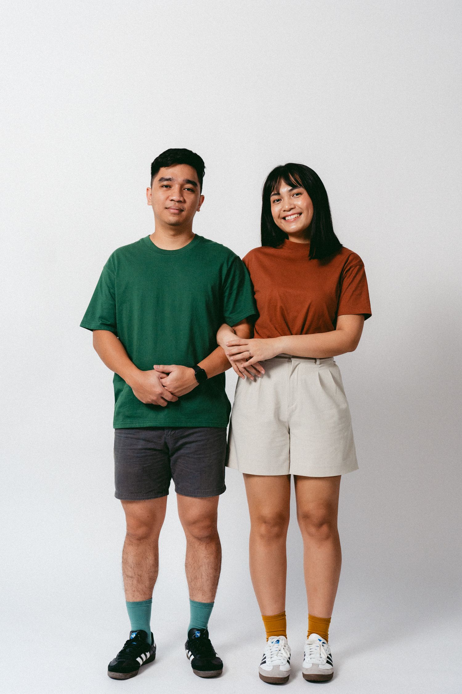 Couple in green and brown shirts pose together against white studio background.