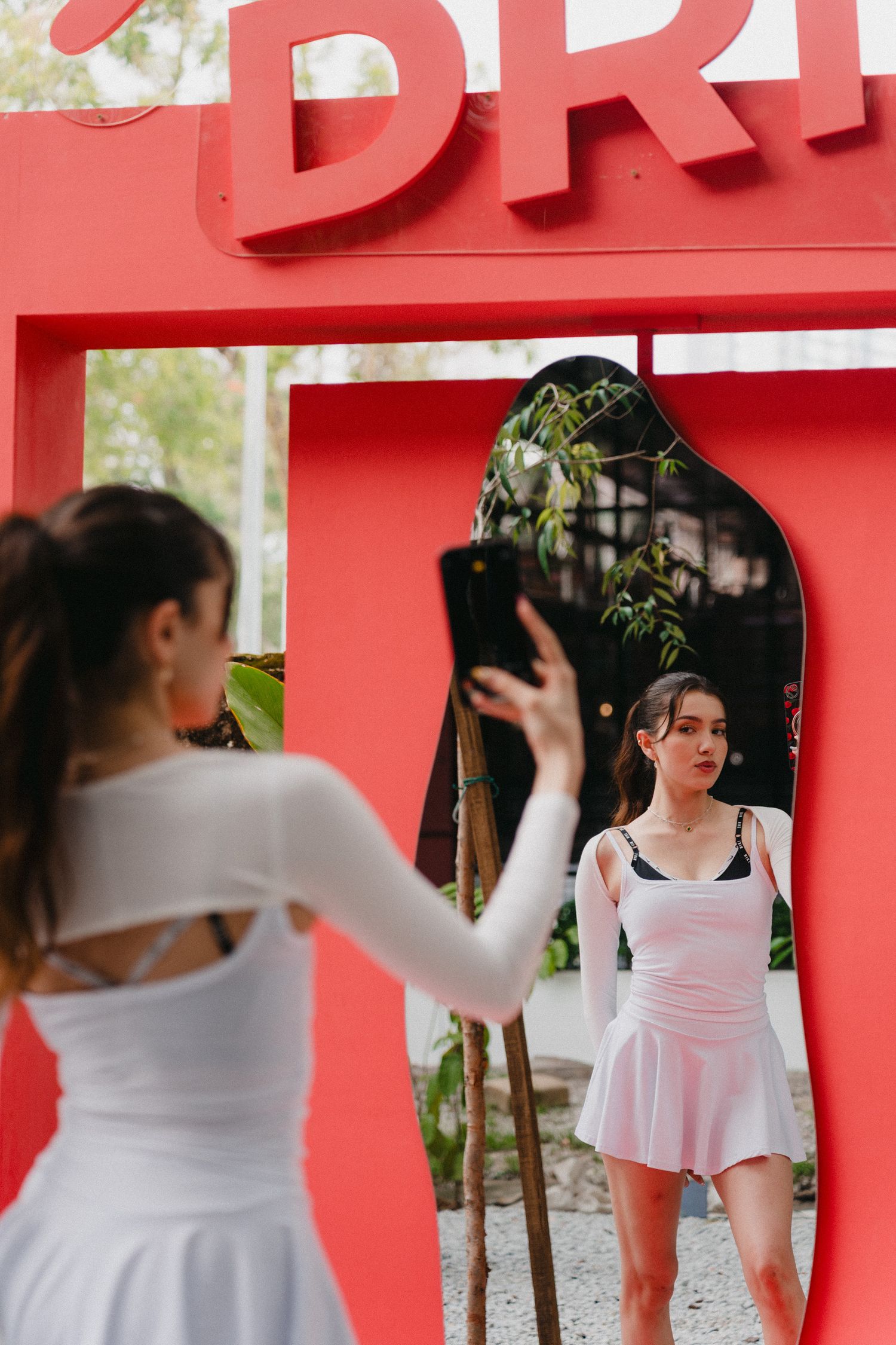A person in a white dress poses in front of a red architectural backdrop in a photo series.