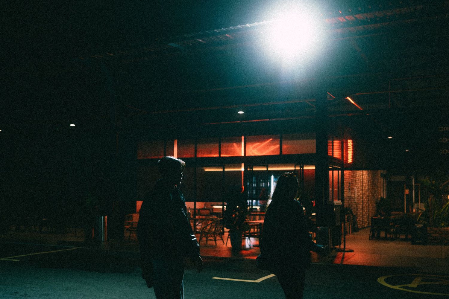 Silhouettes of two people standing outside a dimly lit storefront at night.