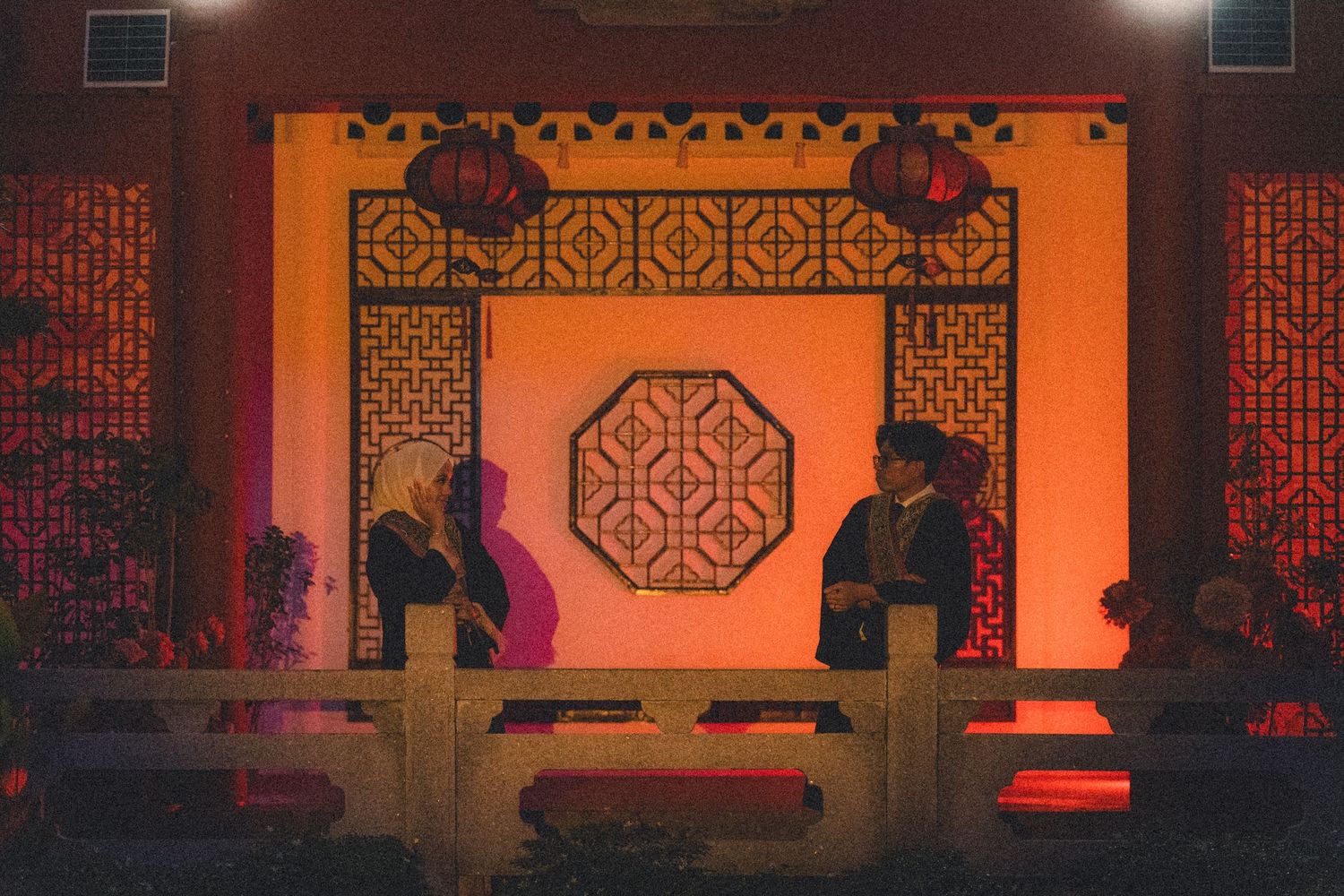 Two silhouettes perform on an orange-lit stage with traditional Asian architectural elements.