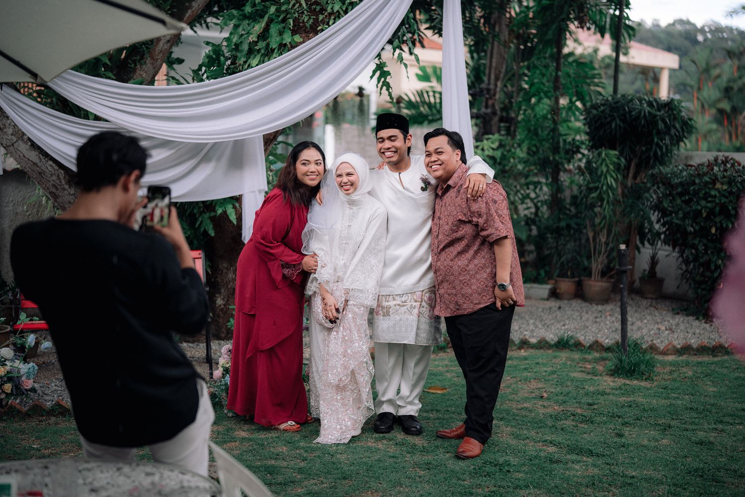 A wedding photo session outdoors with a couple in white attire posing with guests while a photographer captures the moment.