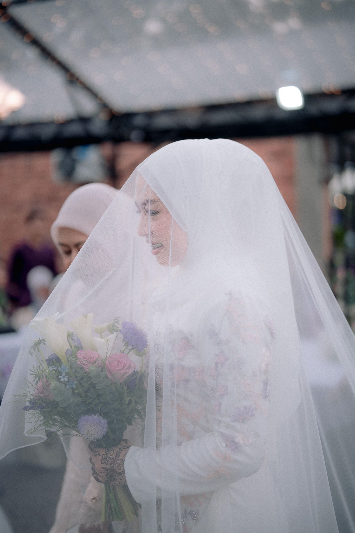 Muslim bride in white hijab and veil holding colorful bouquet of flowers at wedding ceremony.
