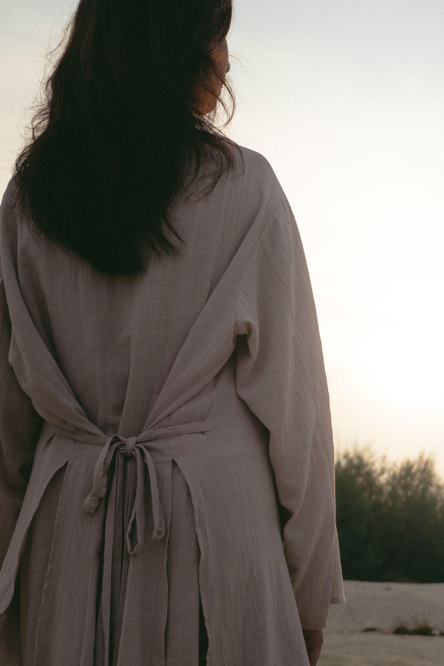 Back view of grey tied robe silhouetted against sunset sky.
