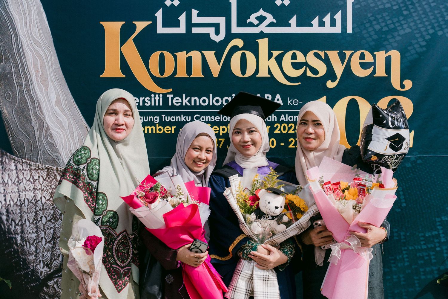 A group wearing traditional Islamic dress poses together with pink and white floral bouquets.