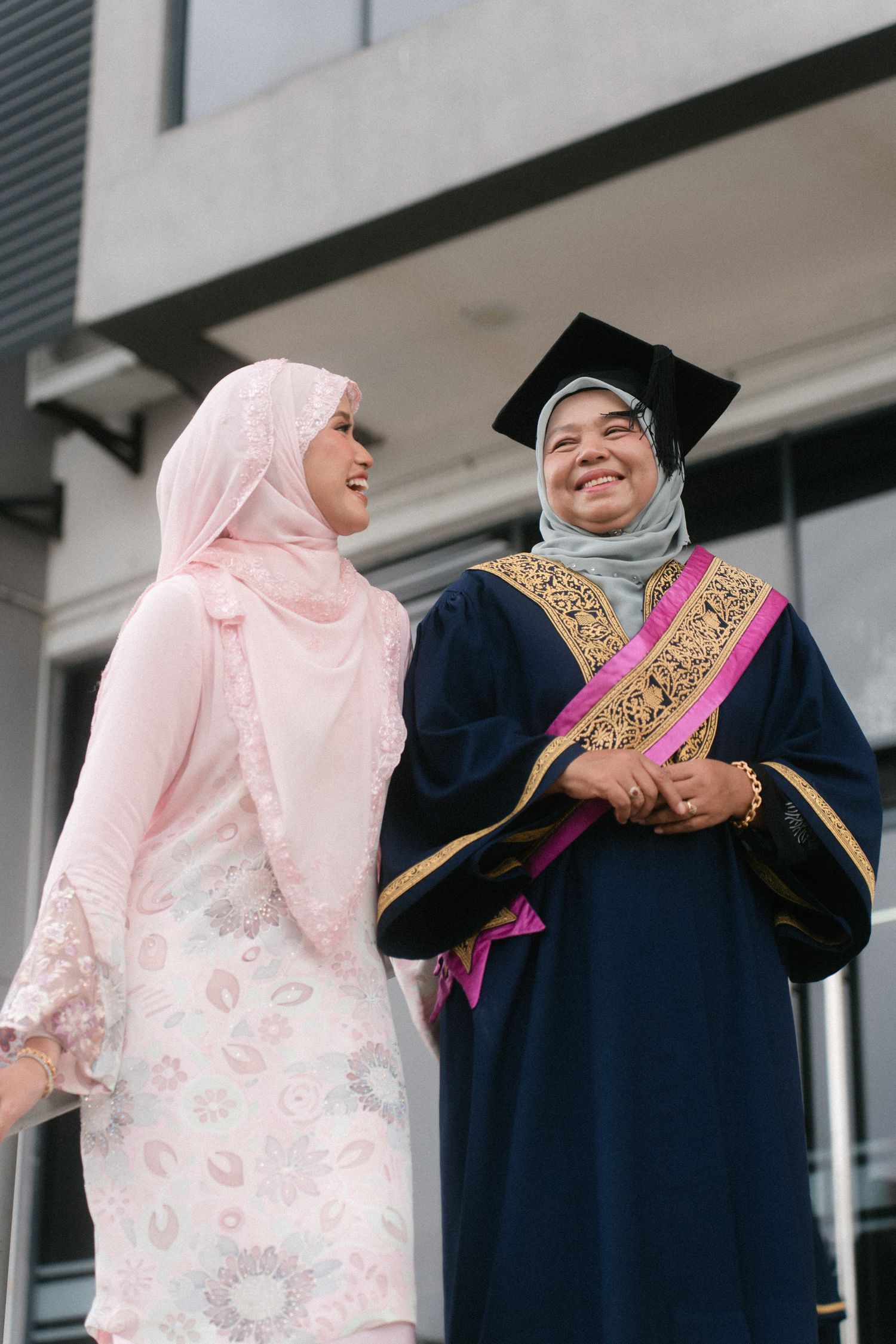 Two people in graduation attire and traditional dress share a joyful moment during a commencement ceremony.