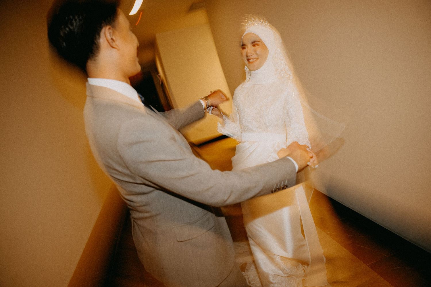 Couple in grey suit and white wedding dress holding hands during intimate indoor ceremony.
