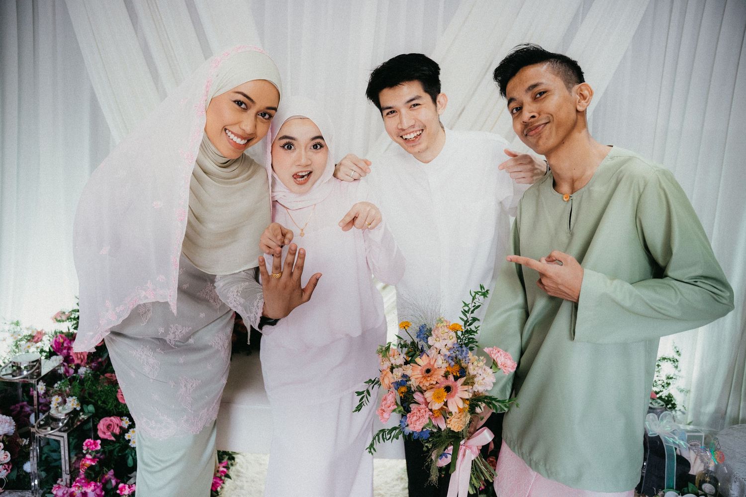 Group of friends pose together at a celebration with floral decorations against a white backdrop.