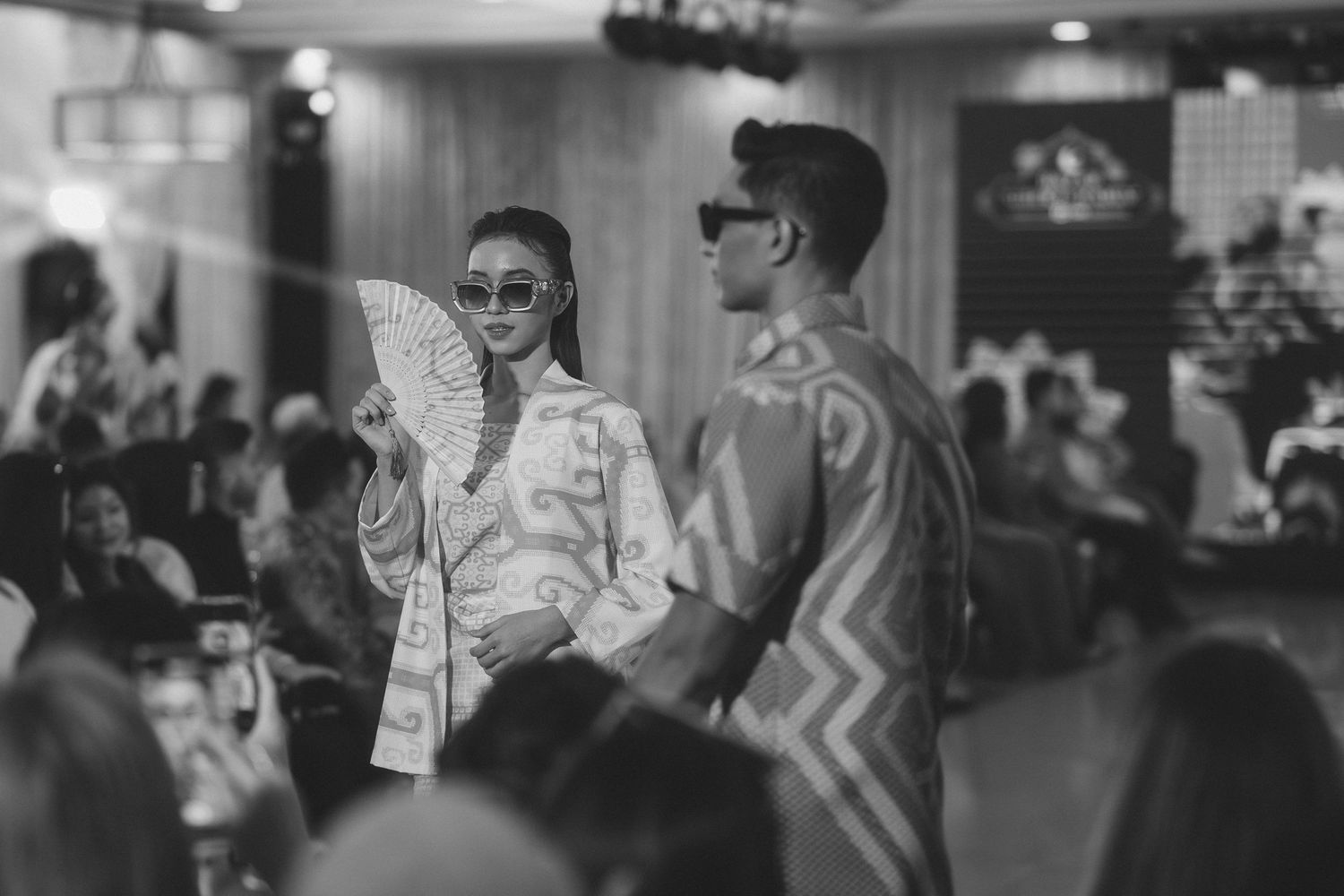 Black and white photo of models in traditional Asian-inspired fashion on runway.