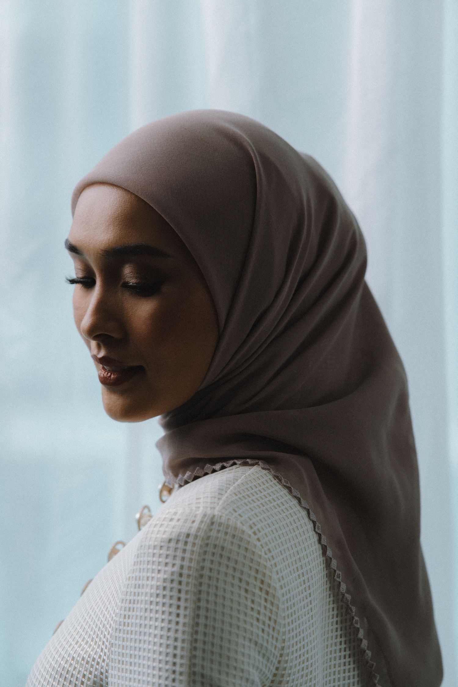 Profile view showing brown hijab and white textured clothing against light background.