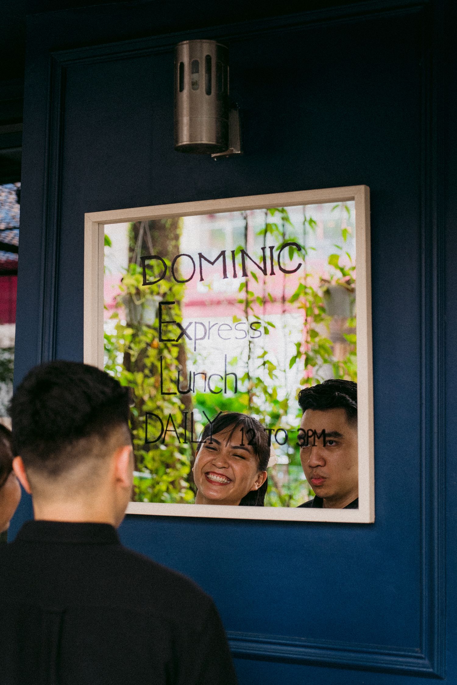 Window view of Dominic cafe signage with people reflected in glass.