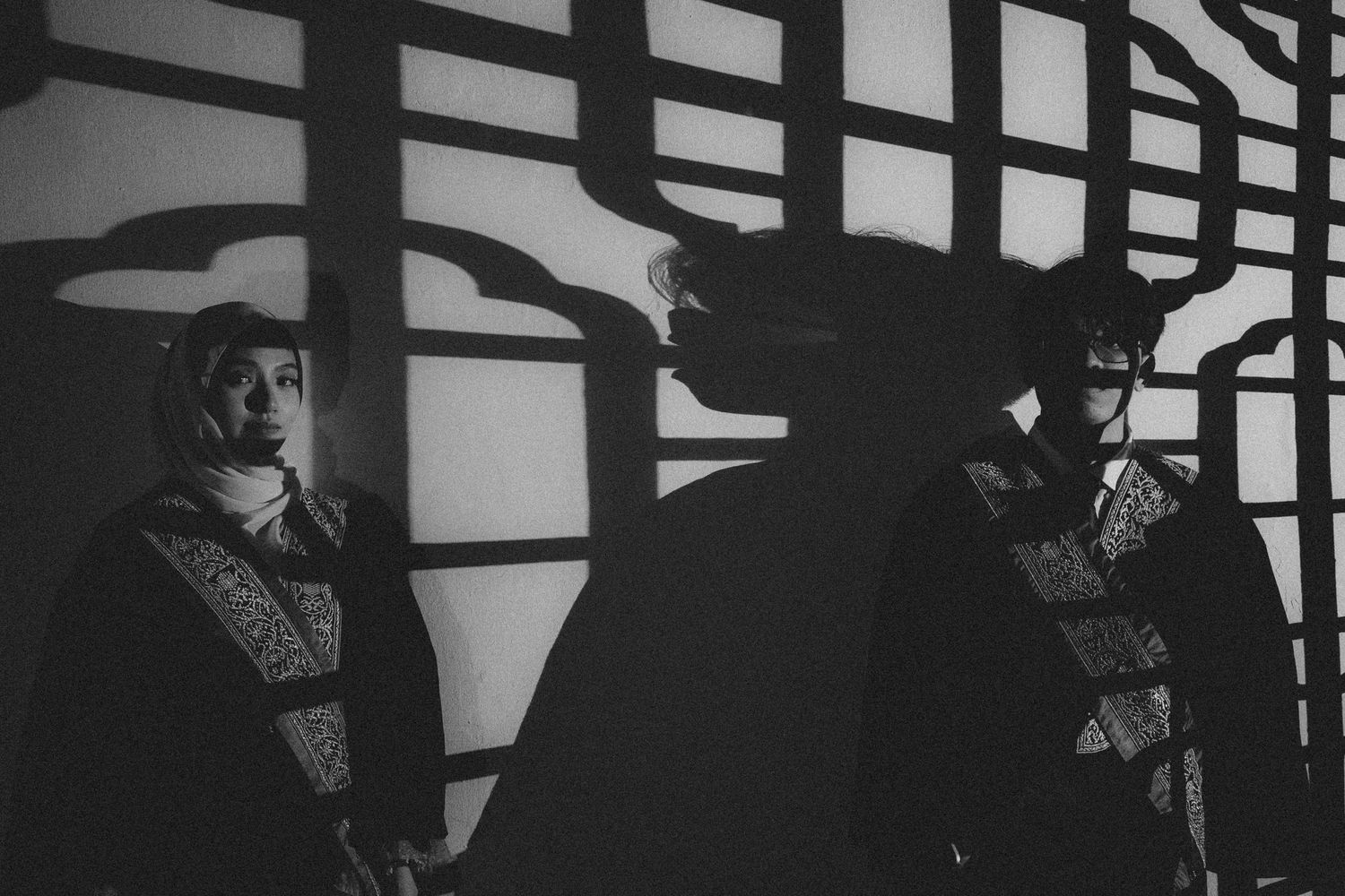 Silhouettes of figures cast dramatic shadows against geometric patterns on a wall.