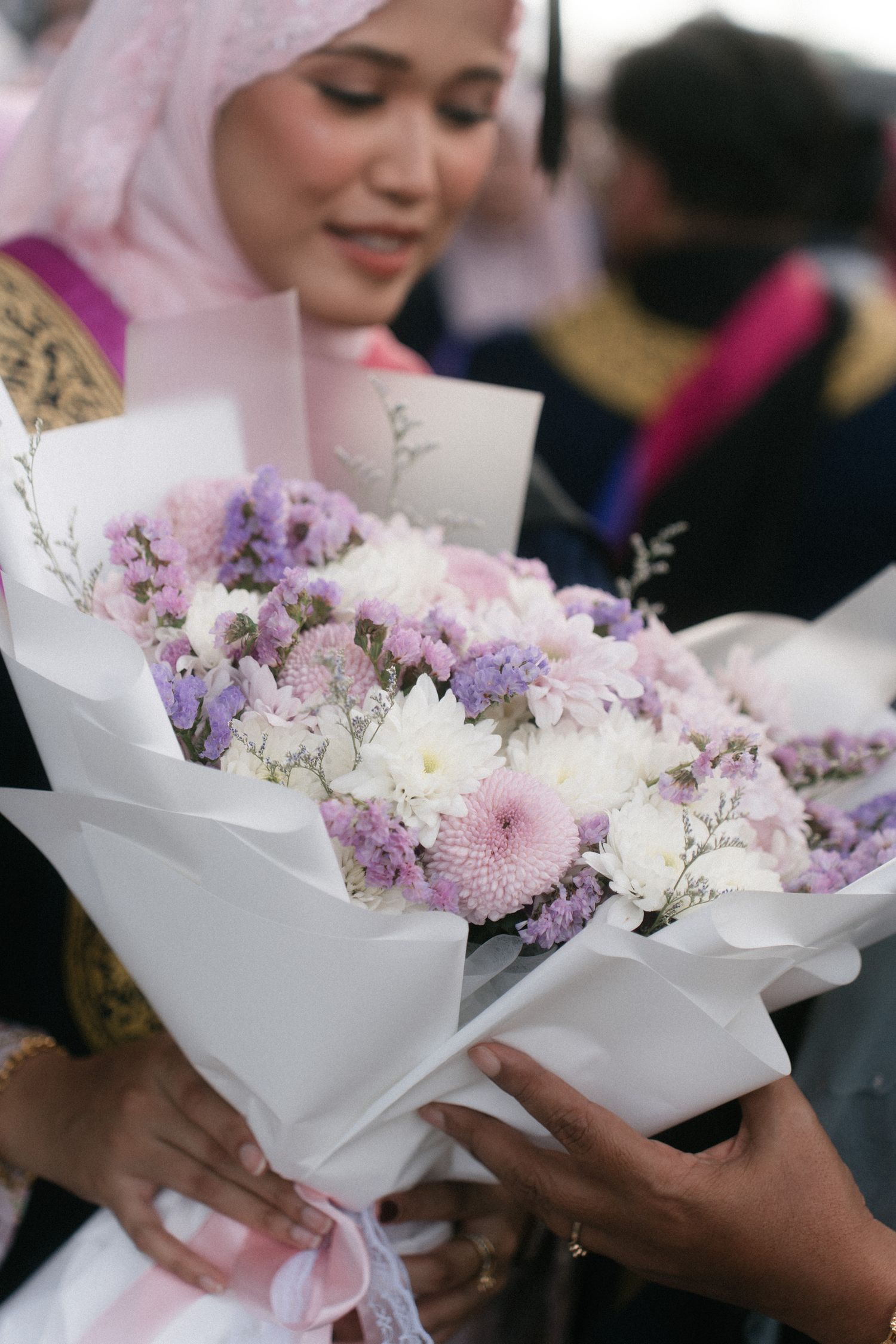 A beautiful bouquet of pink and purple flowers wrapped in white paper being held at a special occasion.