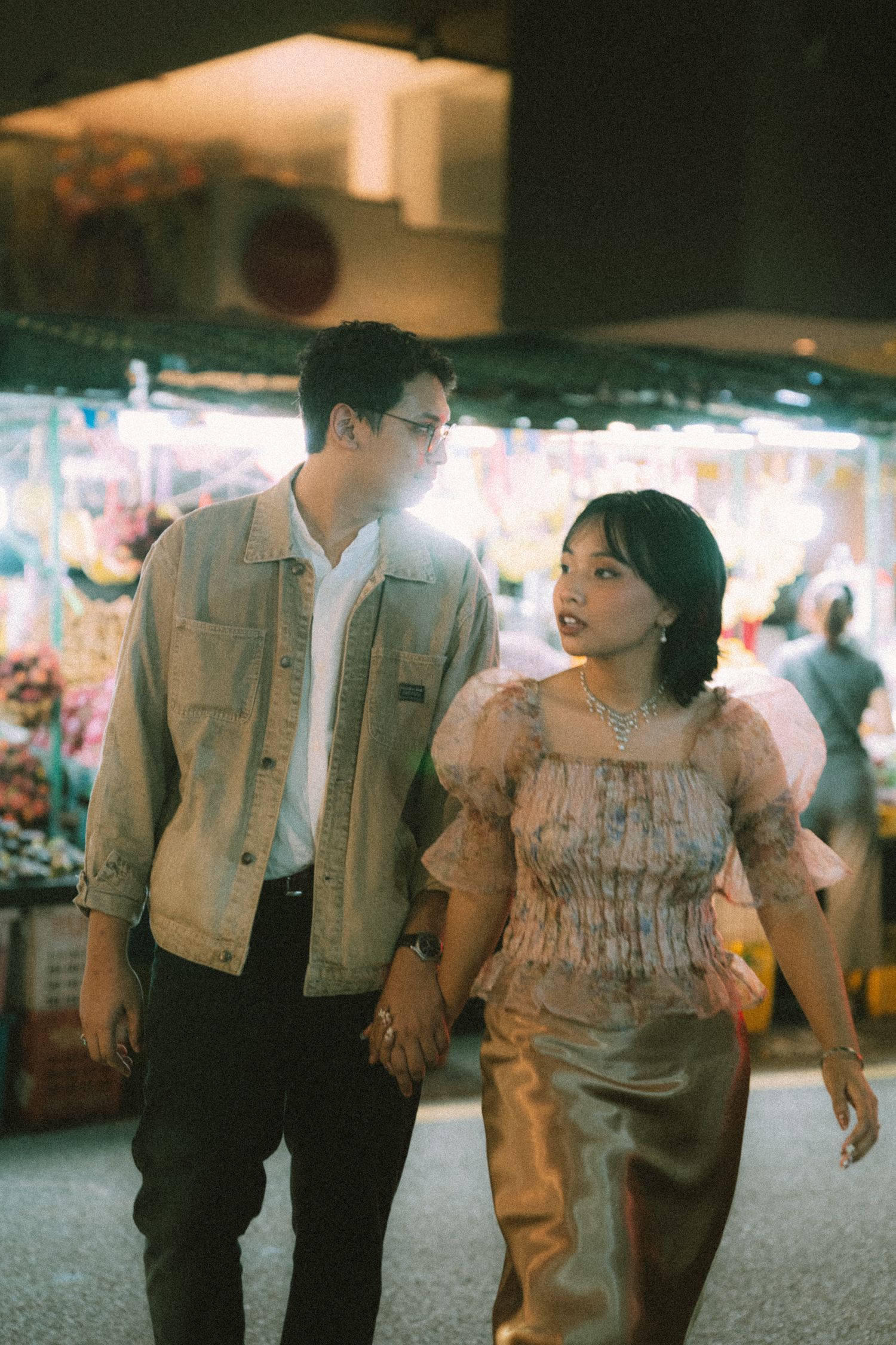 Couple walking through a night market with warm lighting and vendors in background.