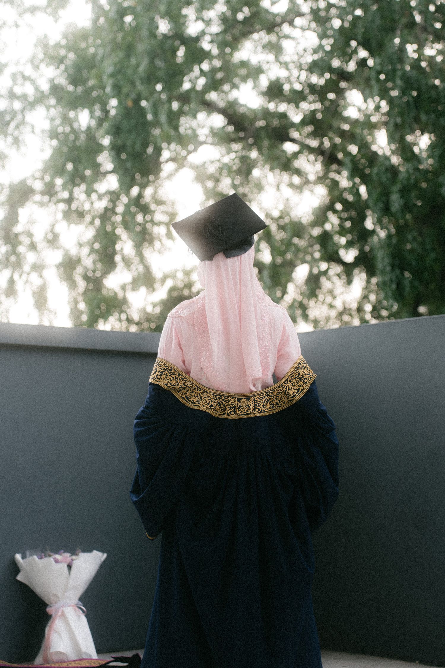 Elegant dress detail showing pink pleated top with black skirt and gold embellished neckline against outdoor backdrop.