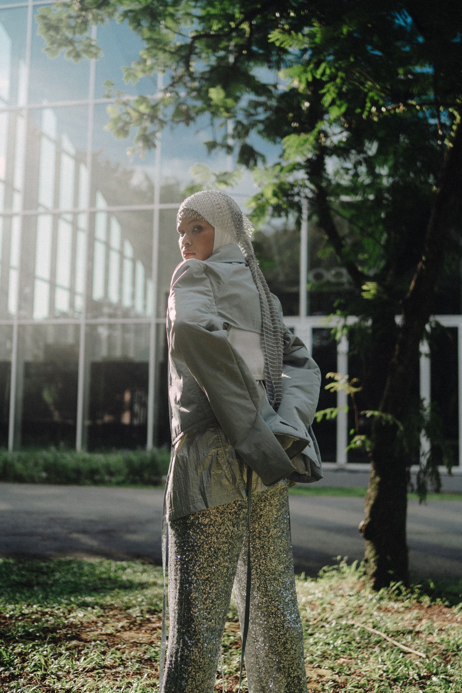 Fashion model in casual grey outfit poses outdoors near modern building.