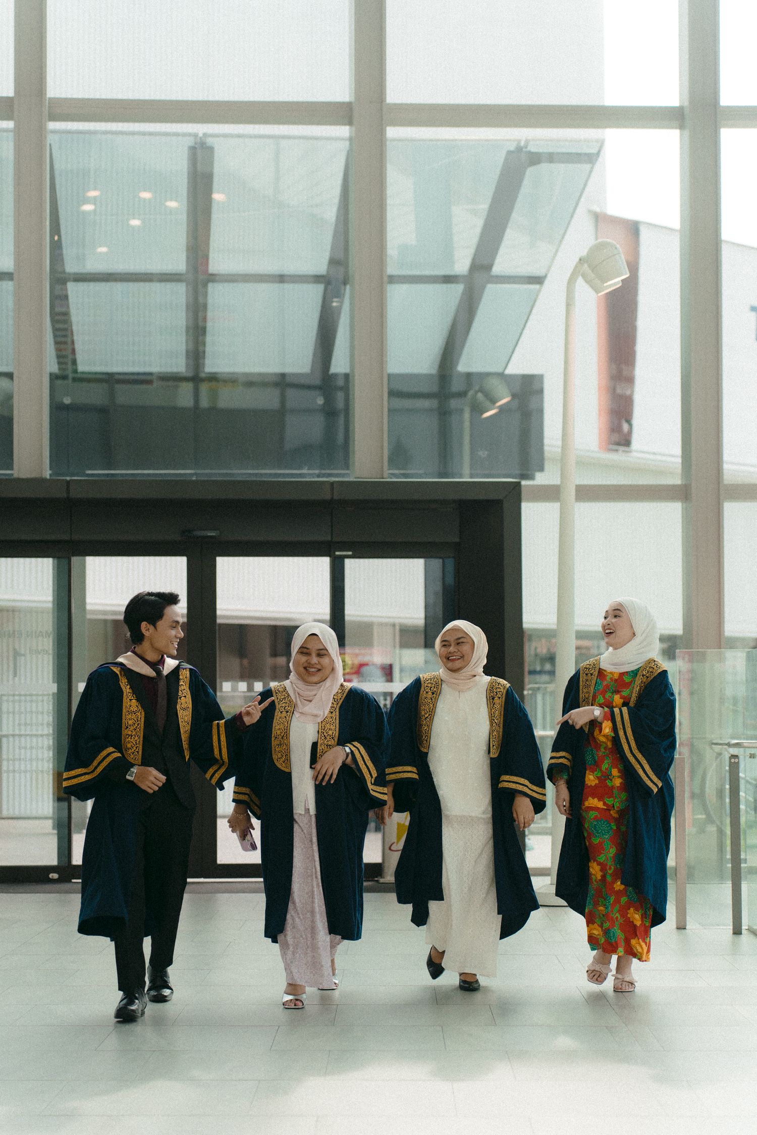 Graduates walking together in academic regalia through a modern building corridor.