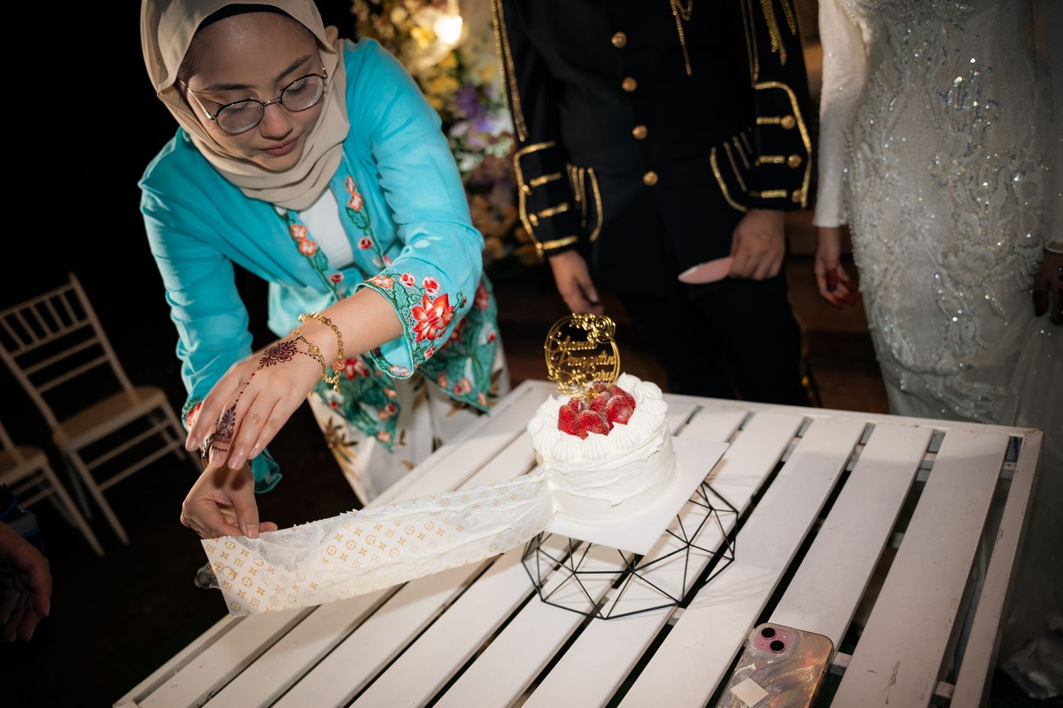 A dessert plate with white frosting and strawberry topping being placed on a white wooden table.