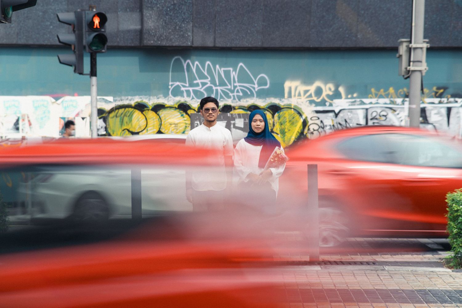 Blurred motion of red car passing by street with graffiti wall and pedestrians.
