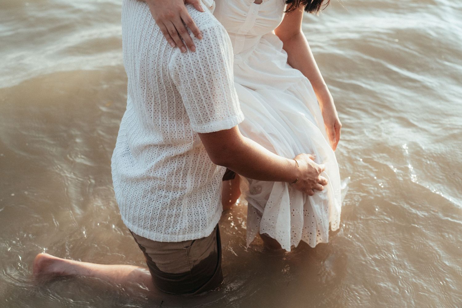 Two people standing together in shallow ocean water at the beach.