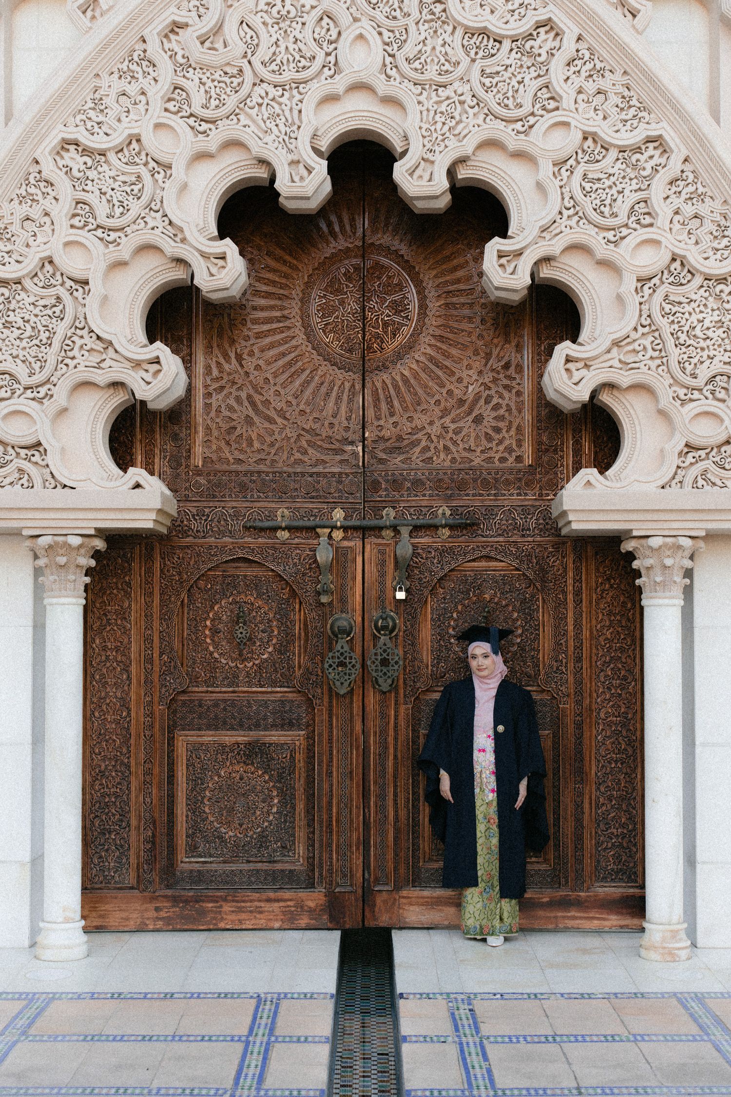Ornate wooden doors with intricate Islamic carvings and white decorative archways in a traditional Moroccan palace.