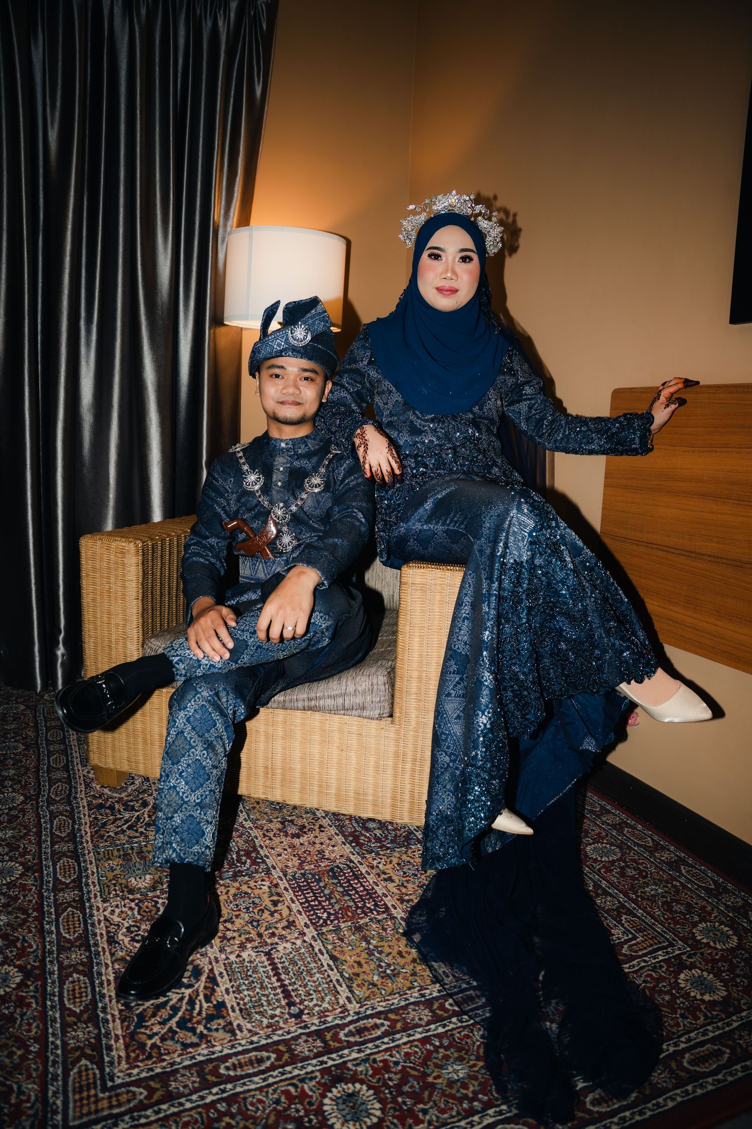 Two people in dark sequined outfits pose elegantly on a patterned rug against dark curtains in coordinated fashion shots.