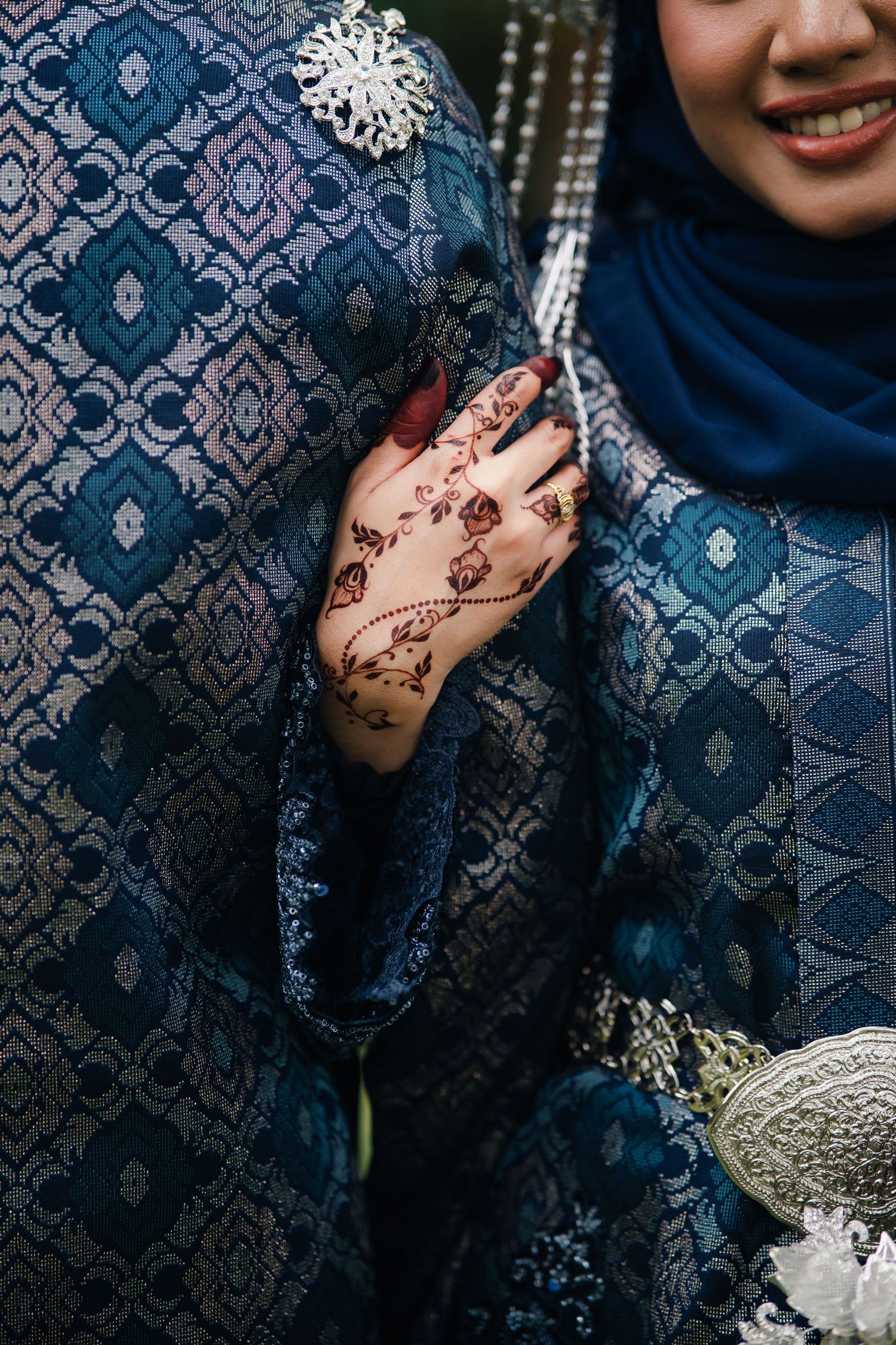Intricate henna design adorns a hand against blue traditional patterned fabric with silver embellishments.