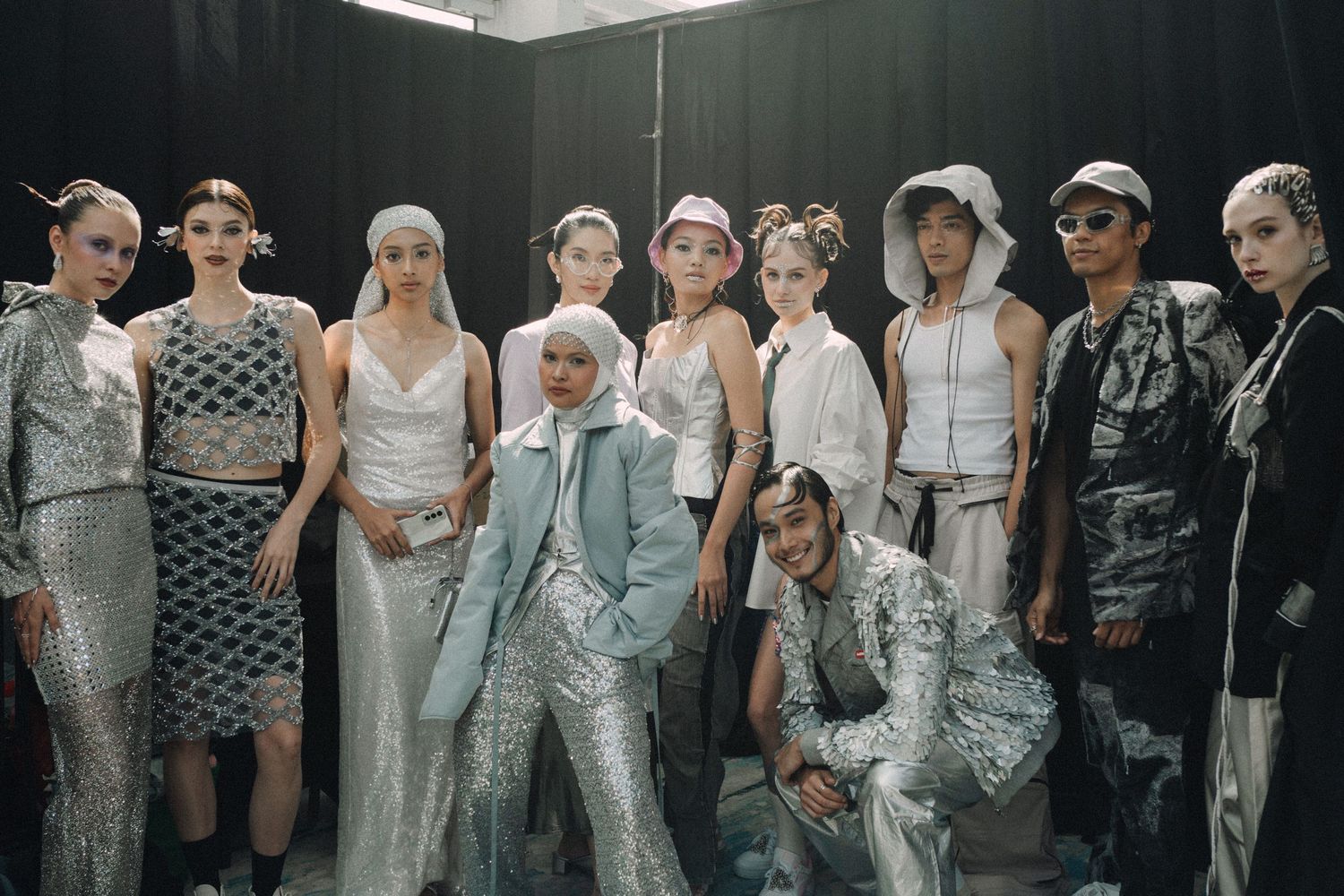 Group photo of models wearing avant-garde silver and white fashion collection backstage.