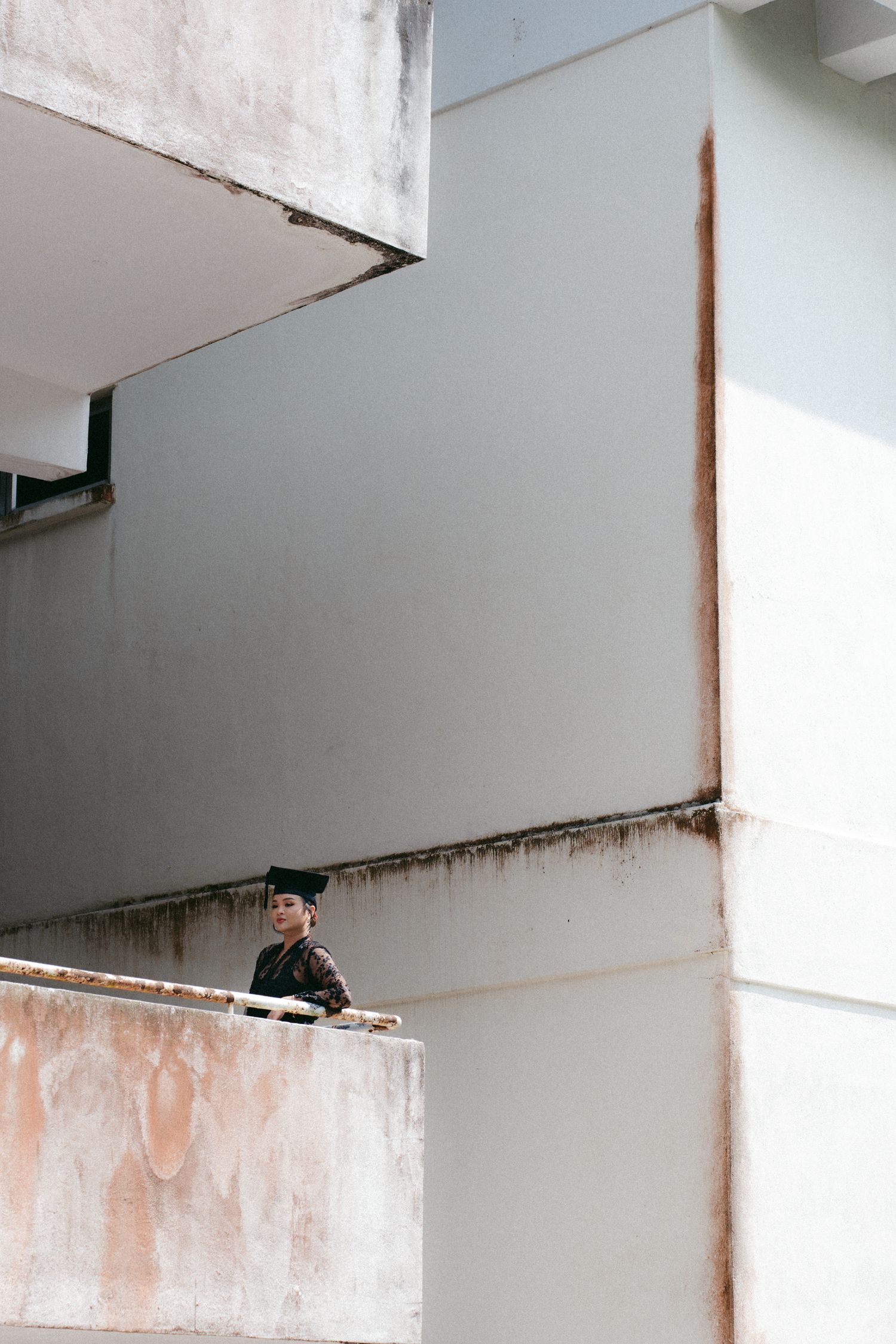 A person stands on a weathered concrete balcony of a minimalist white building with rustic details.