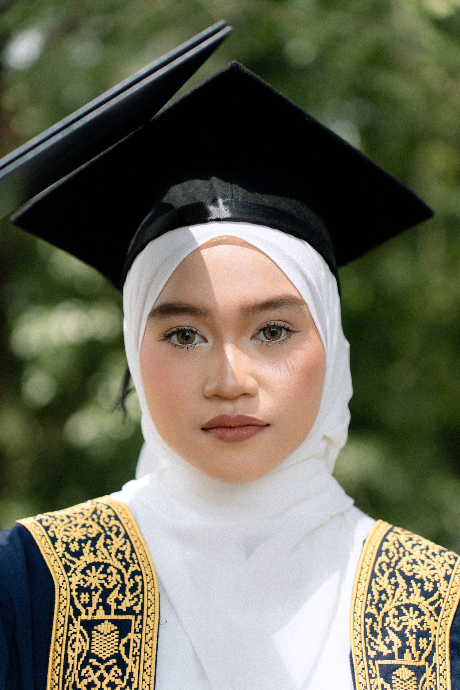 Graduate wearing traditional white hijab and black graduation cap with gold embroidered academic regalia.