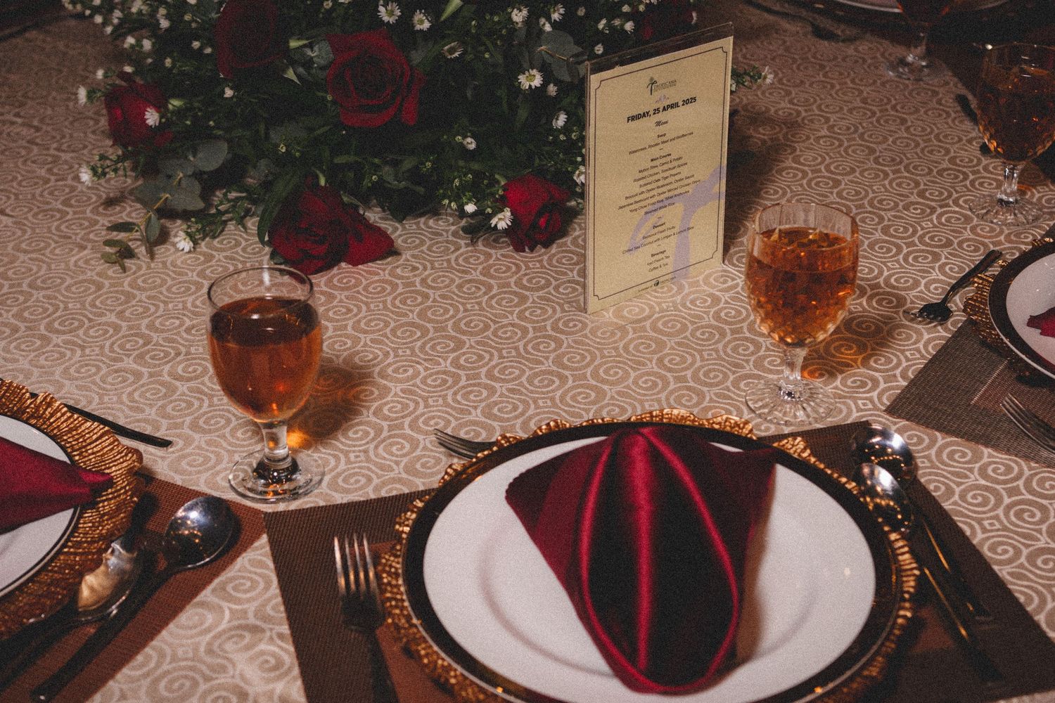 A formal holiday table setting with red and green napkin, wine glasses, and Christmas decorations beneath a decorated tree.